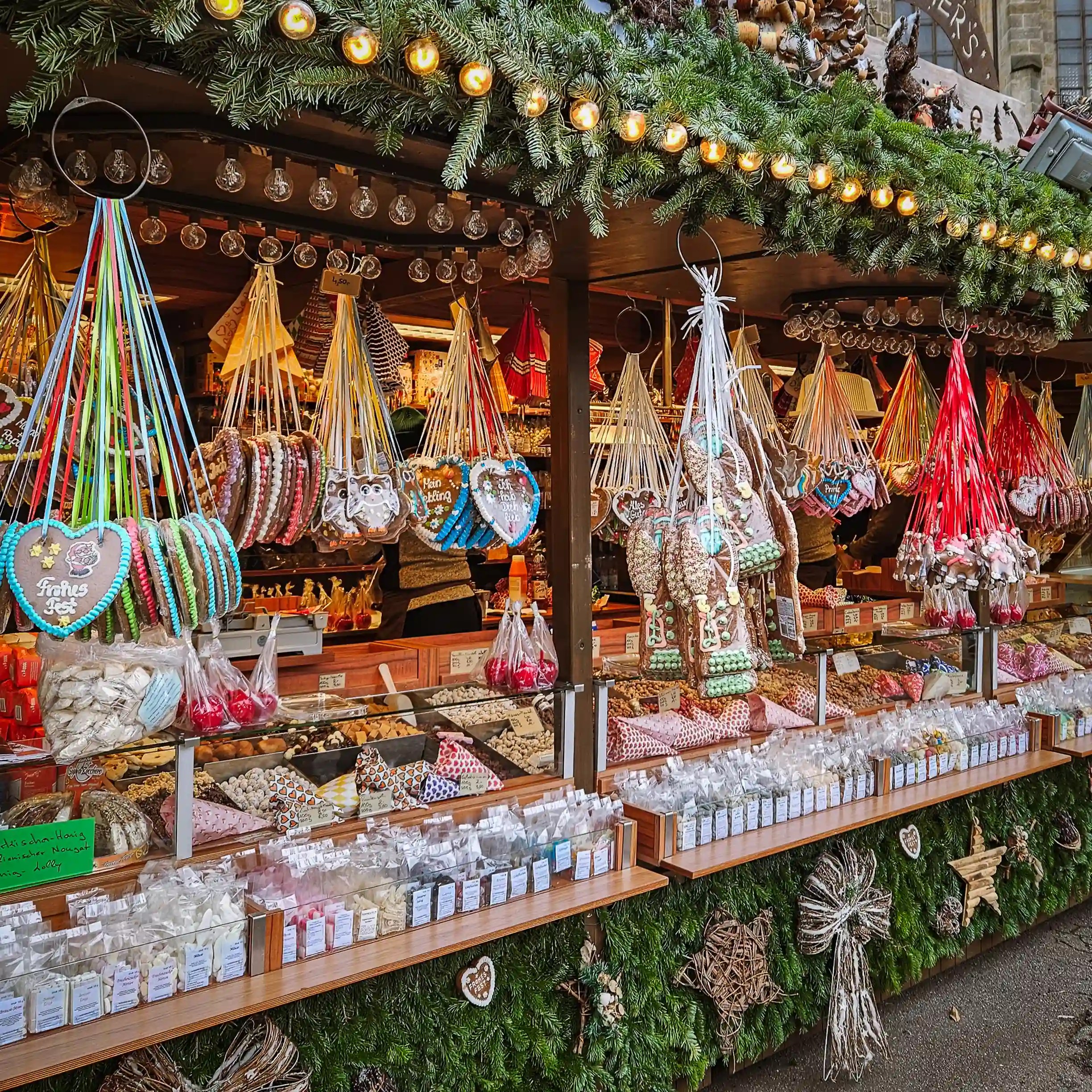 A Christmas market stall filled with hanging gingerbread hearts, candies, and sweets beneath evergreen garlands.