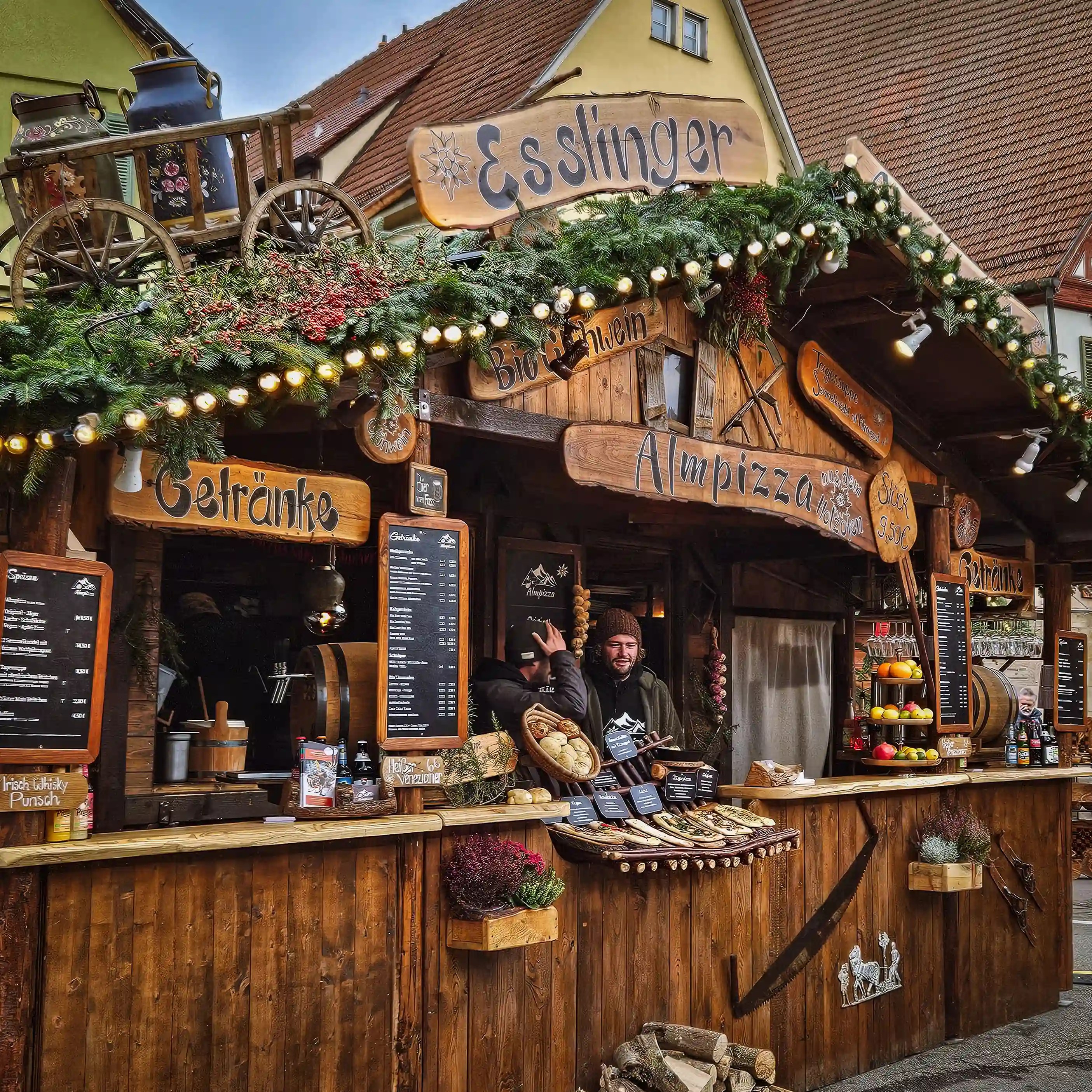 The Esslinger Almpizza and Glühwein stall decorated with pine branches and wooden signs at the Esslingen Christmas Market.