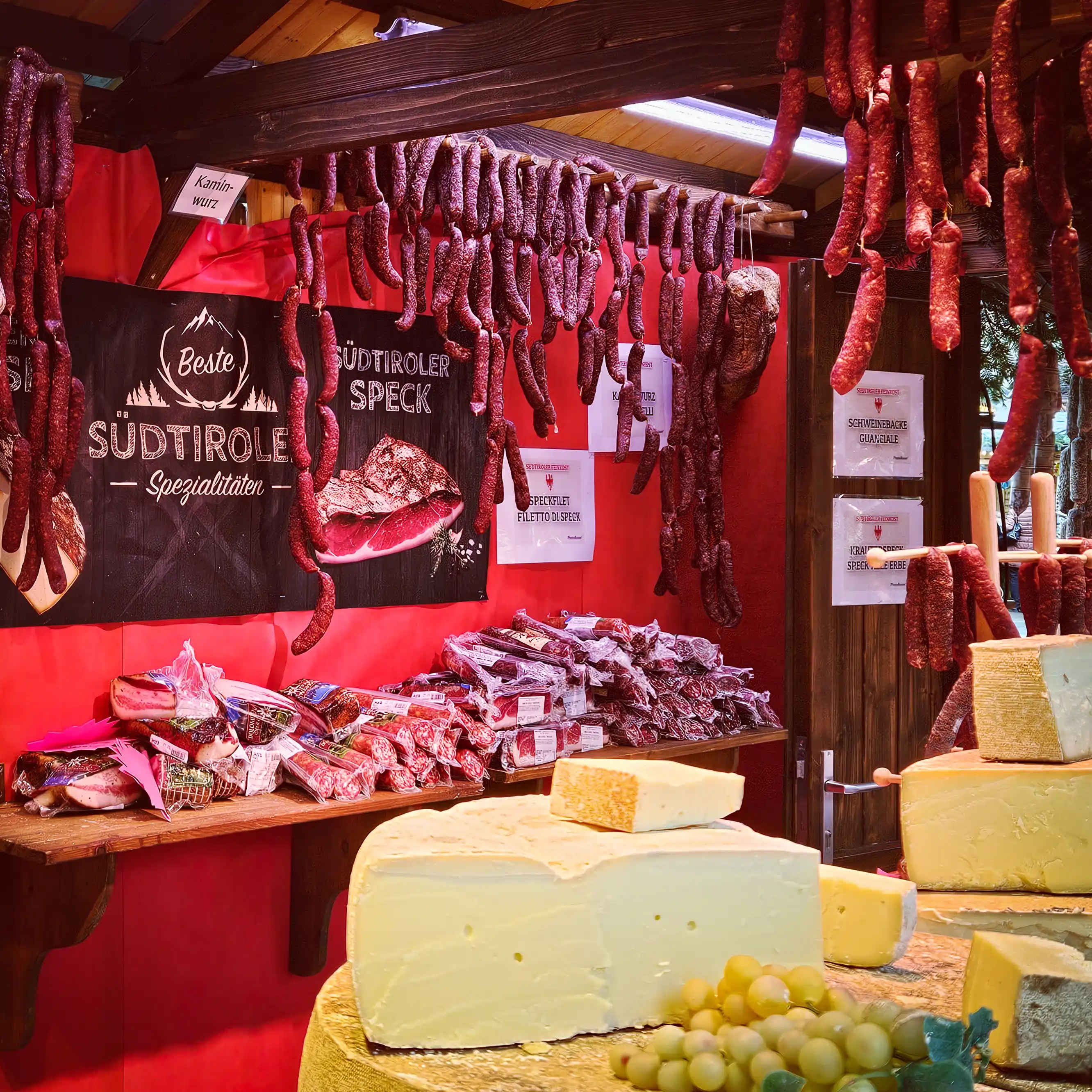 A South Tyrolean specialties stall displaying hanging sausages, speck, and large cheese wheels at the Esslingen Christmas Market.