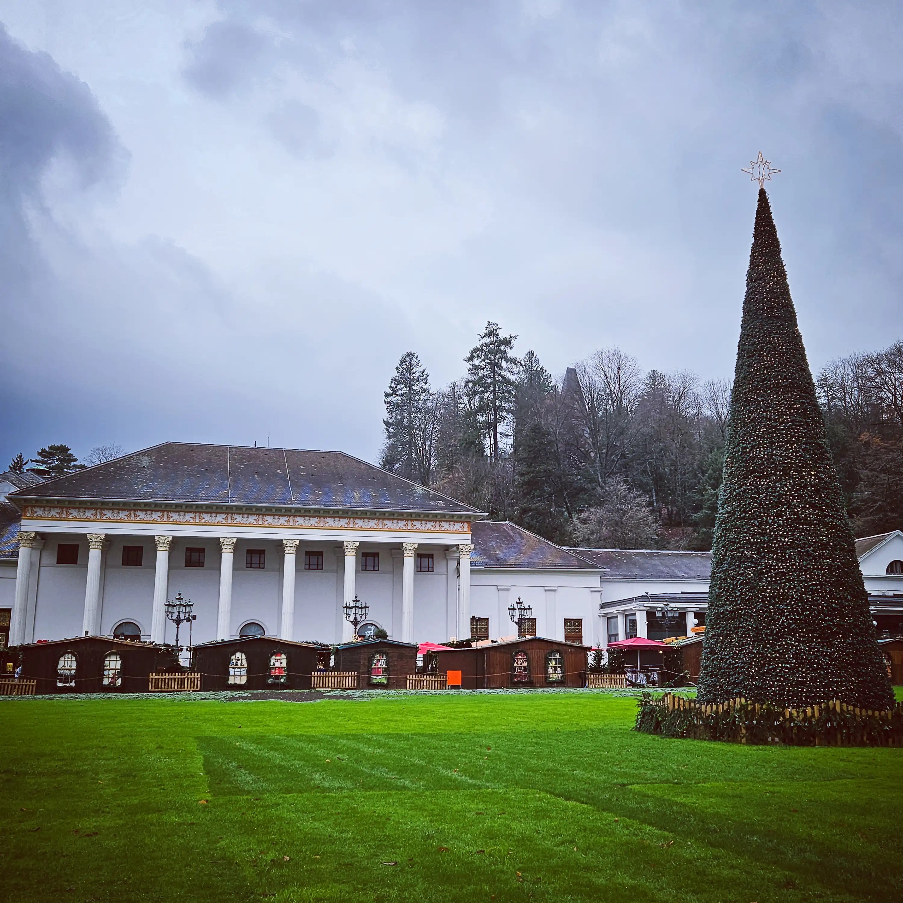 Large white Kurhaus building with columns and a tall Christmas tree on the lawn in Baden-Baden.