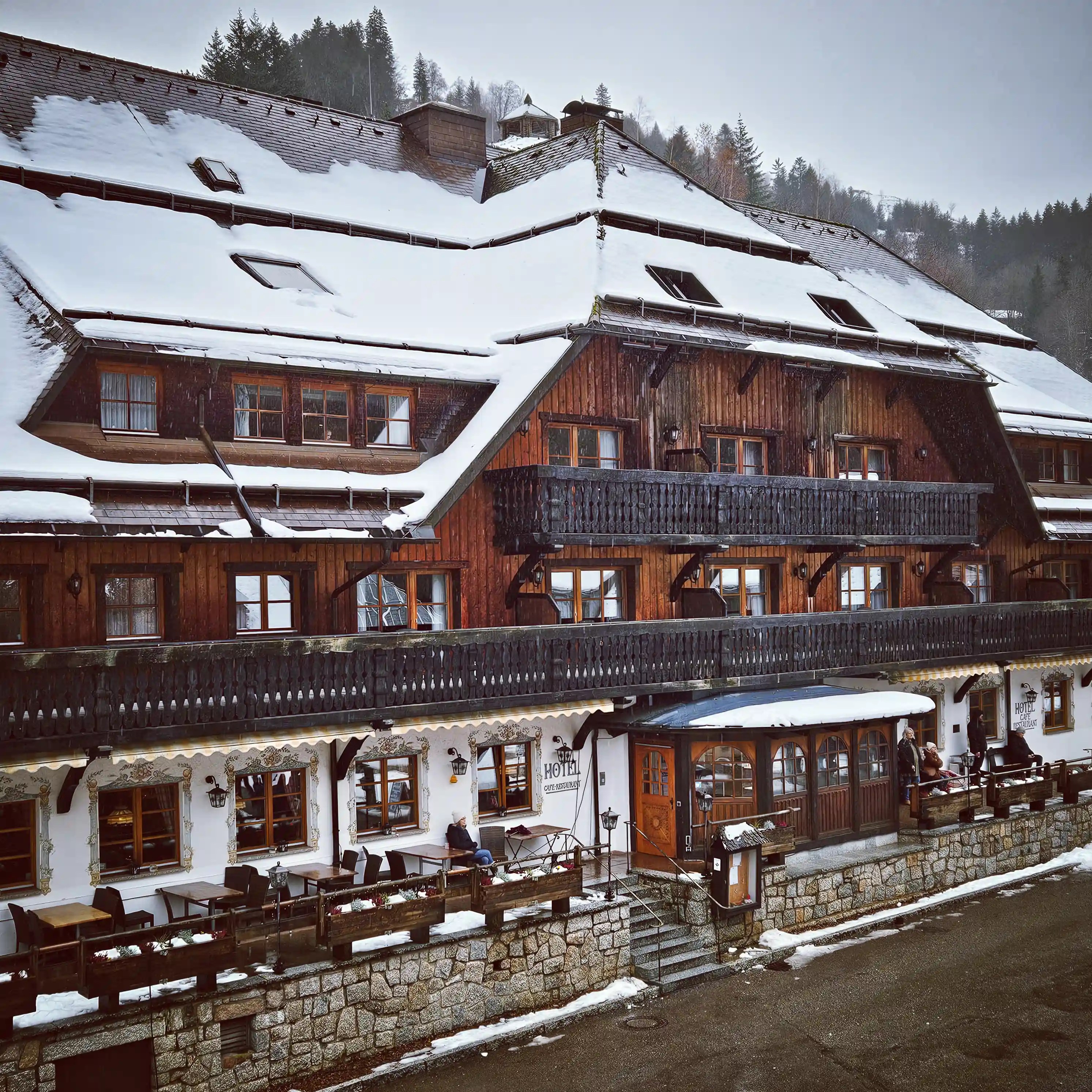 Snow-covered wooden facade of Hotel Hofgut Sternen with balconies and outdoor seating in winter.
