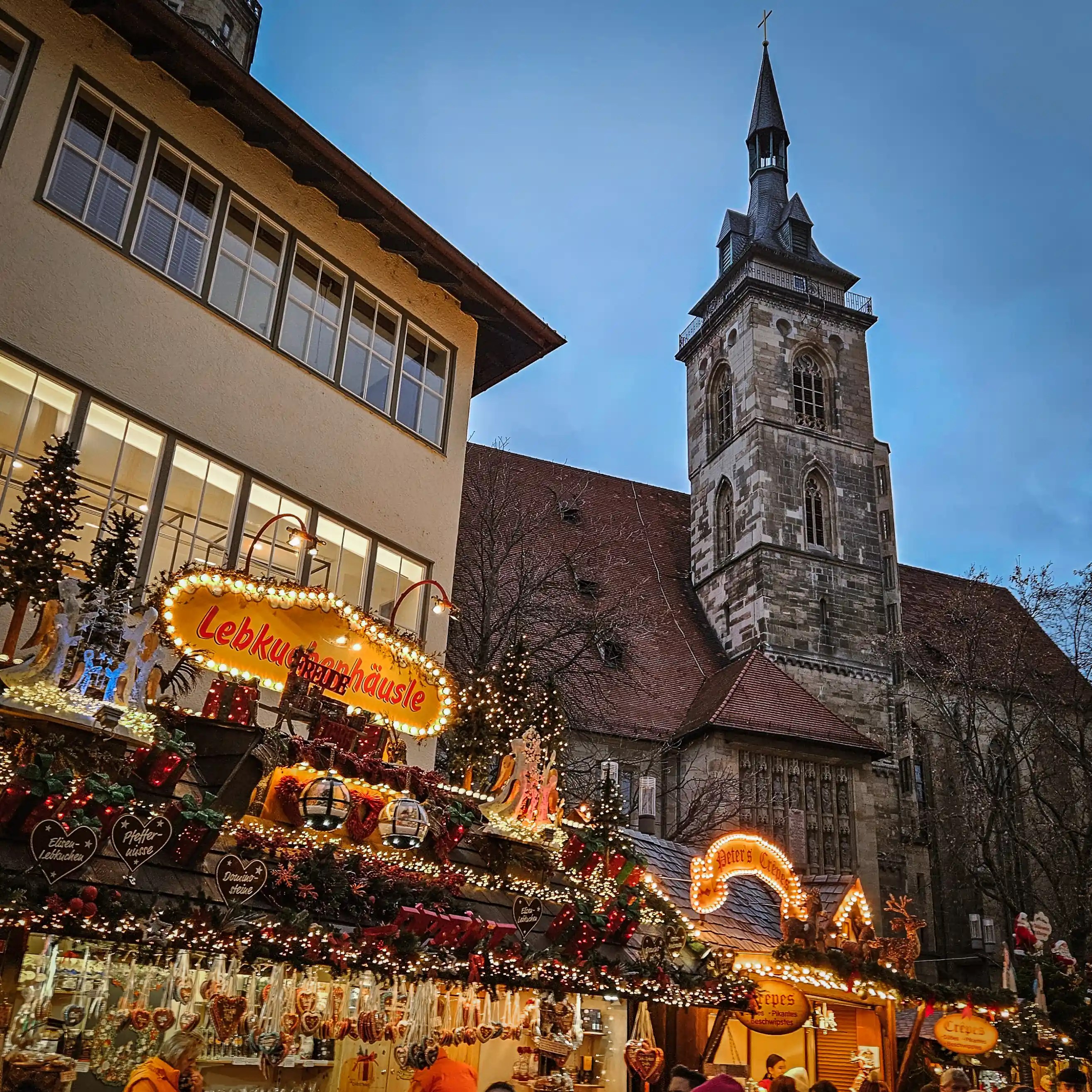 Christmas market stalls decorated with lights and garlands near Stuttgart’s Collegiate Church tower.