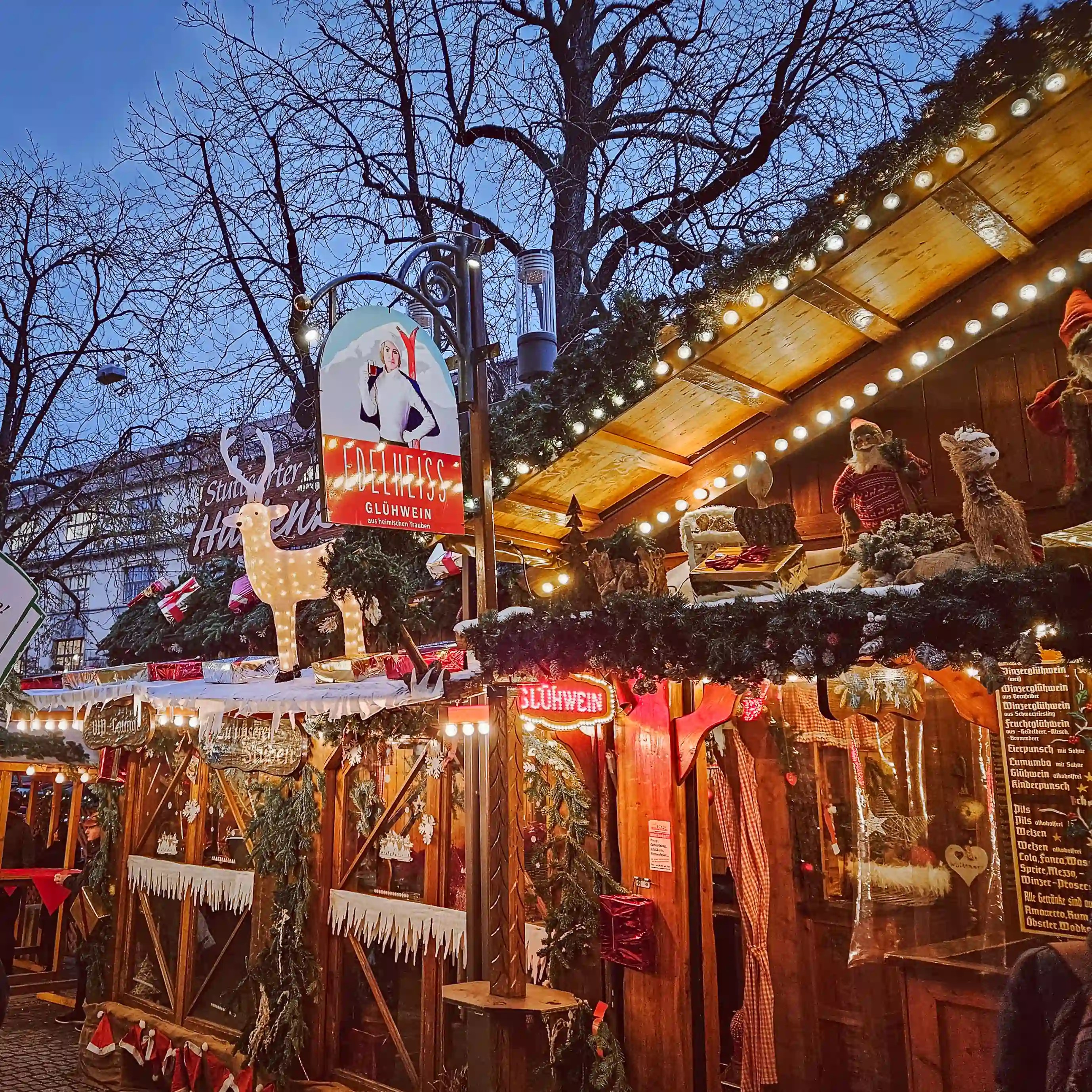 Cozy wooden stall decorated with garlands, reindeer, and glowing lights selling Glühwein at Stuttgart’s Christmas Market.
