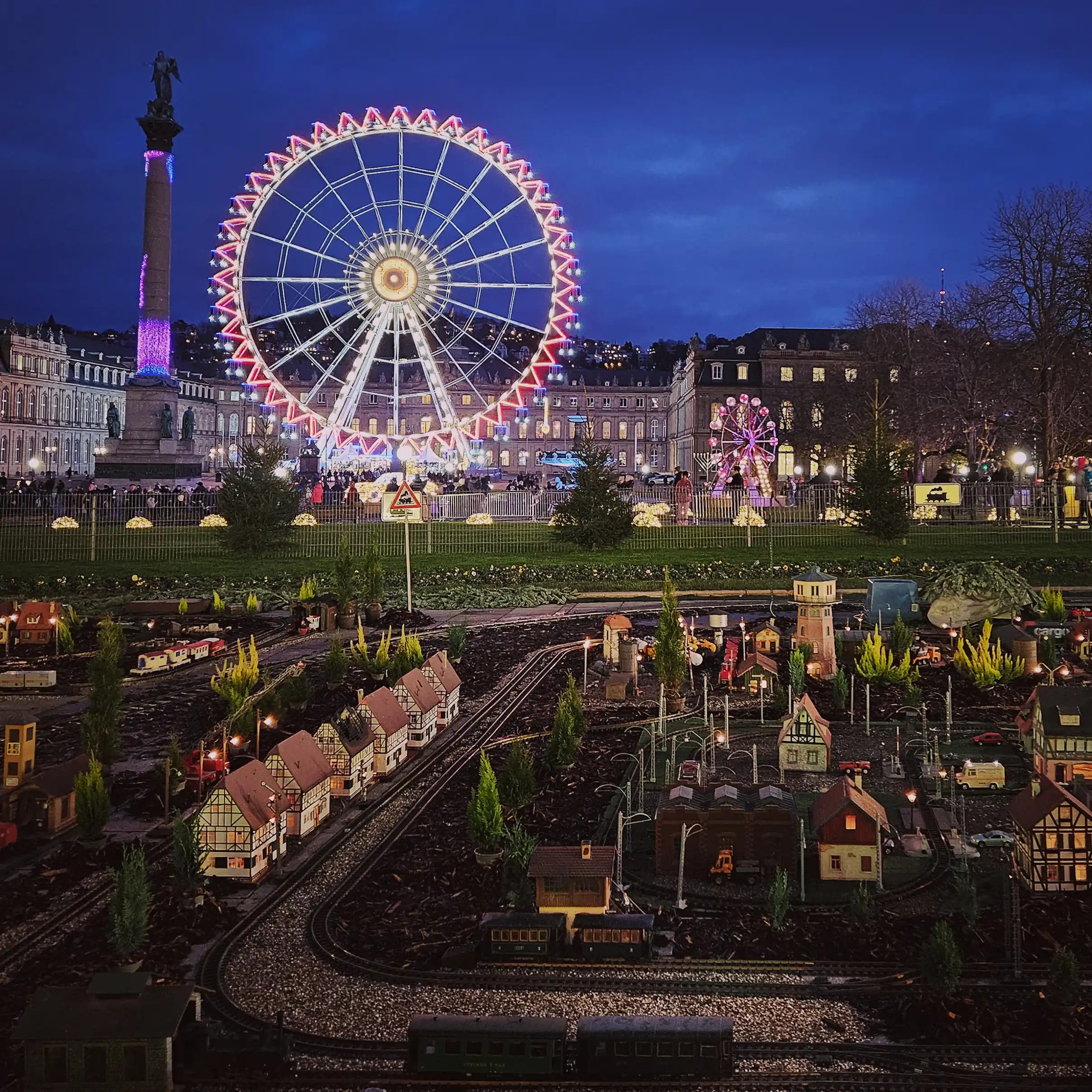 Night view of the Stuttgart Ferris wheel and model train display in Schlossplatz during the Christmas season.