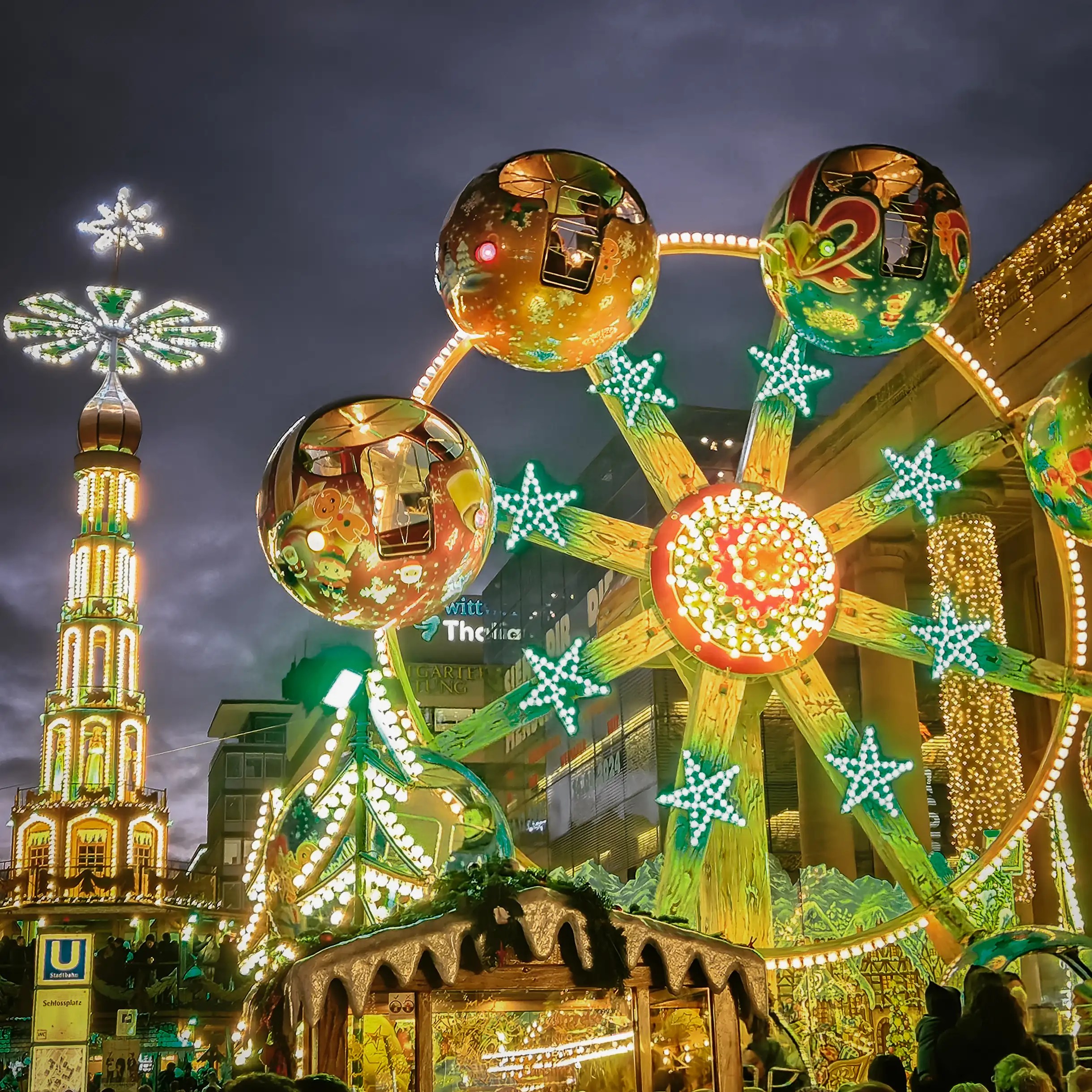 Illuminated Christmas rides, including a Ferris wheel and tall candle tower, at Stuttgart’s market fairground.