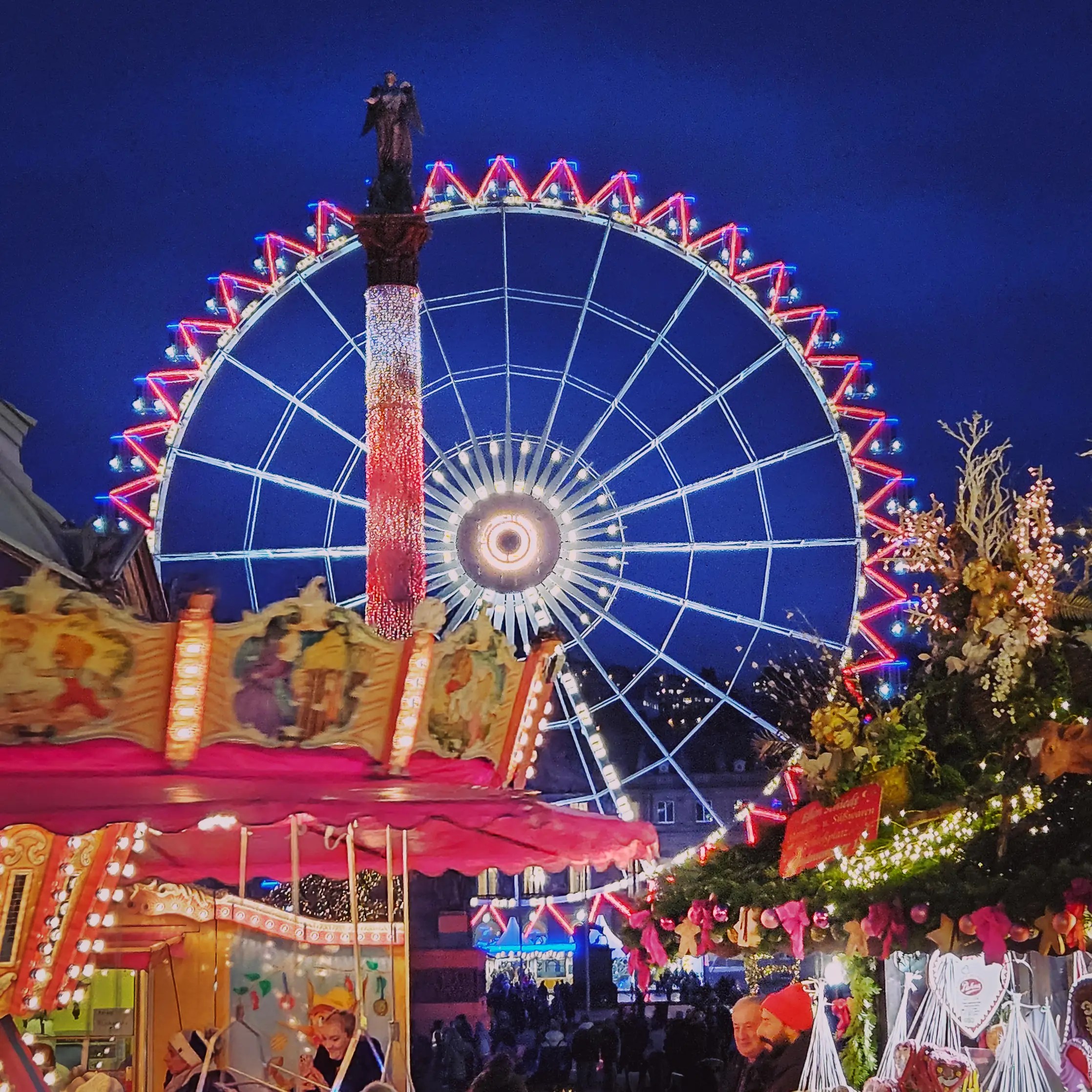 Carousel and Ferris wheel glowing with colorful lights at Stuttgart’s Schlossplatz Christmas Market.