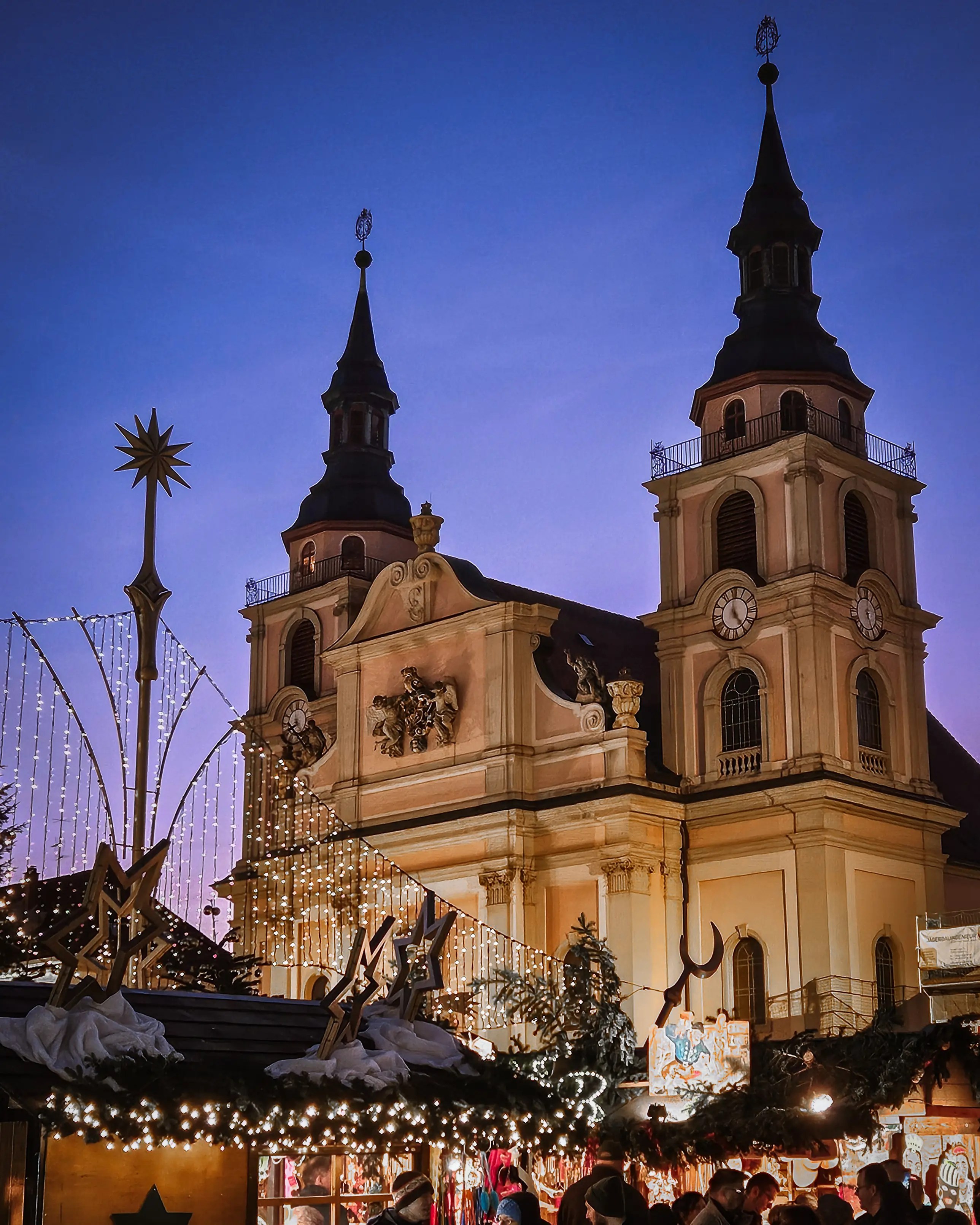 The twin towers of Ludwigsburg’s Protestant City Church illuminated above the Christmas market stalls at blue hour.