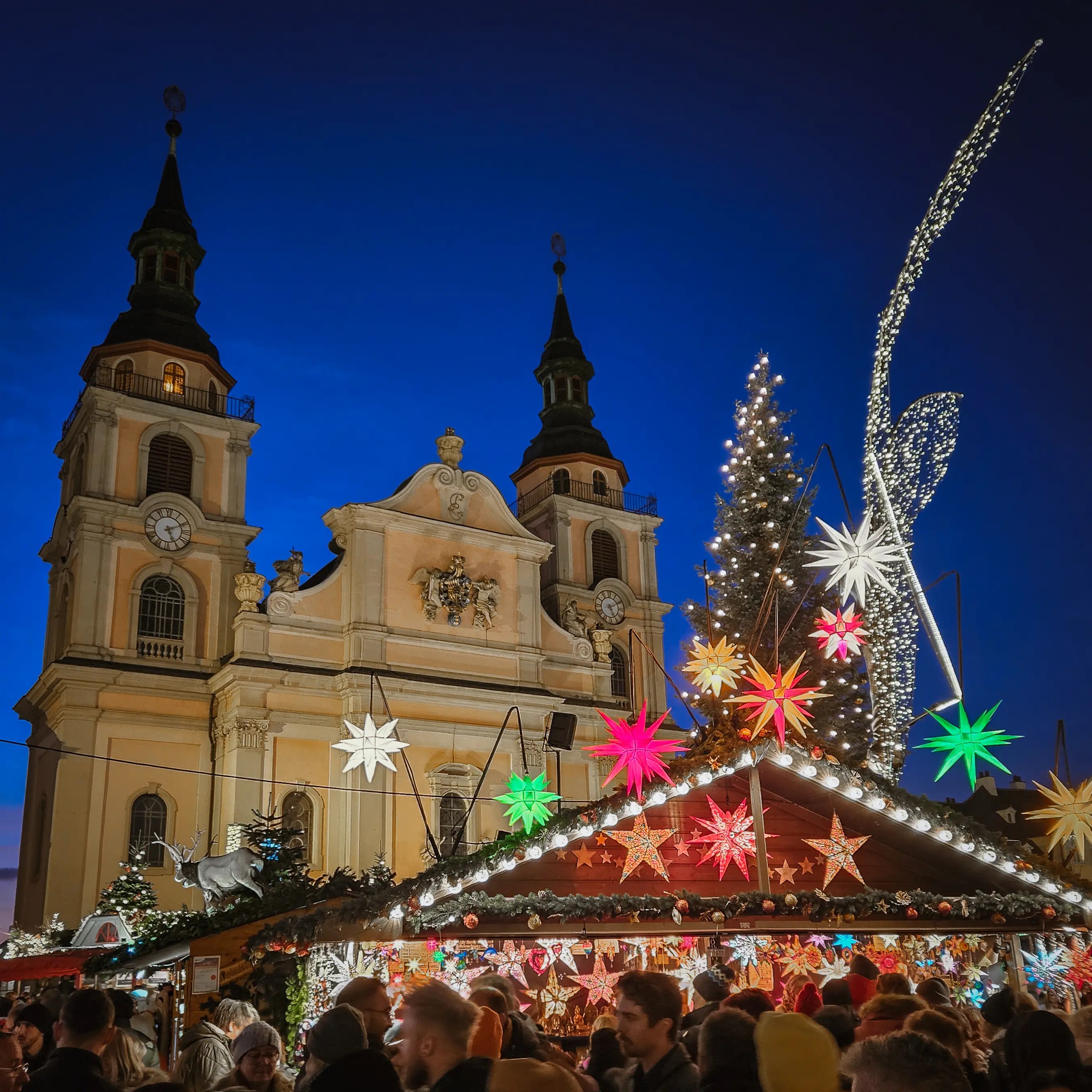 Crowds enjoying the Ludwigsburg Baroque Christmas Market with illuminated stars, Christmas tree, and church towers in the background.