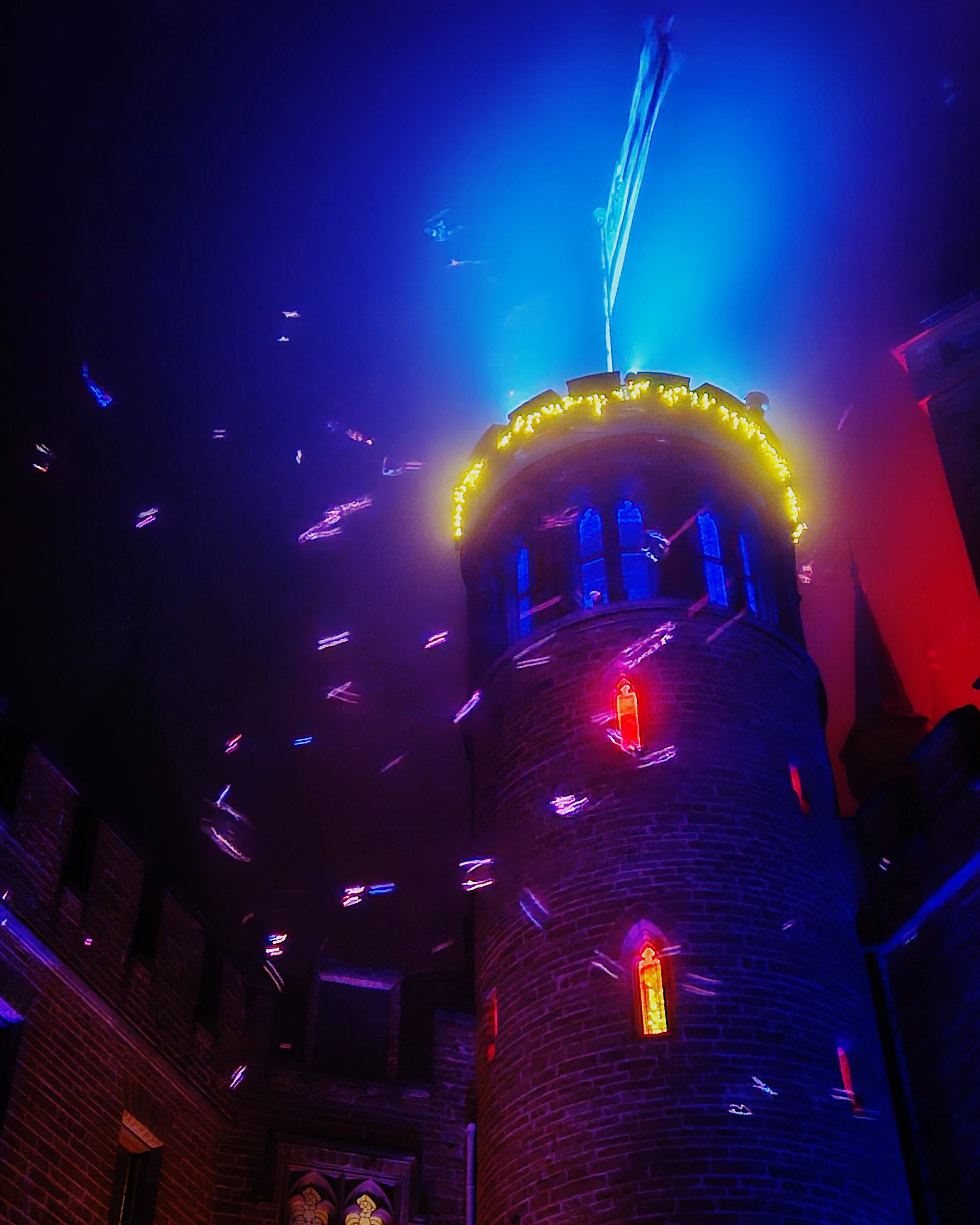Castle tower illuminated in blue and yellow lights with snowflakes at Burg Hohenzollern’s Royal Winter Magic.