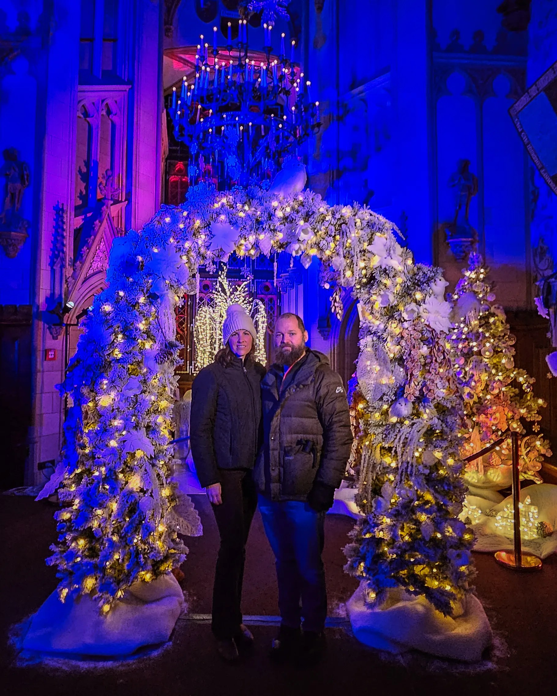 Couple standing beneath an illuminated archway of white garlands and Christmas lights inside Burg Hohenzollern during Royal Winter Magic.