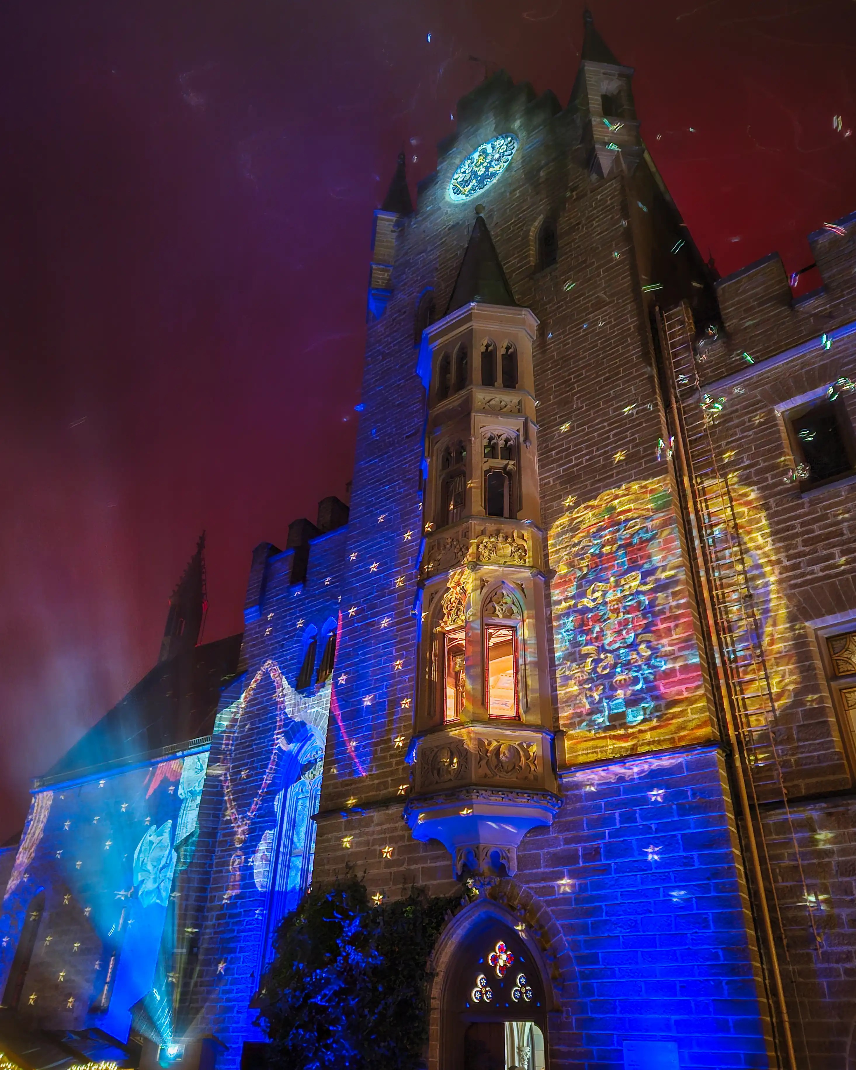Burg Hohenzollern’s tower illuminated with colorful projections and star patterns against a pink night sky.