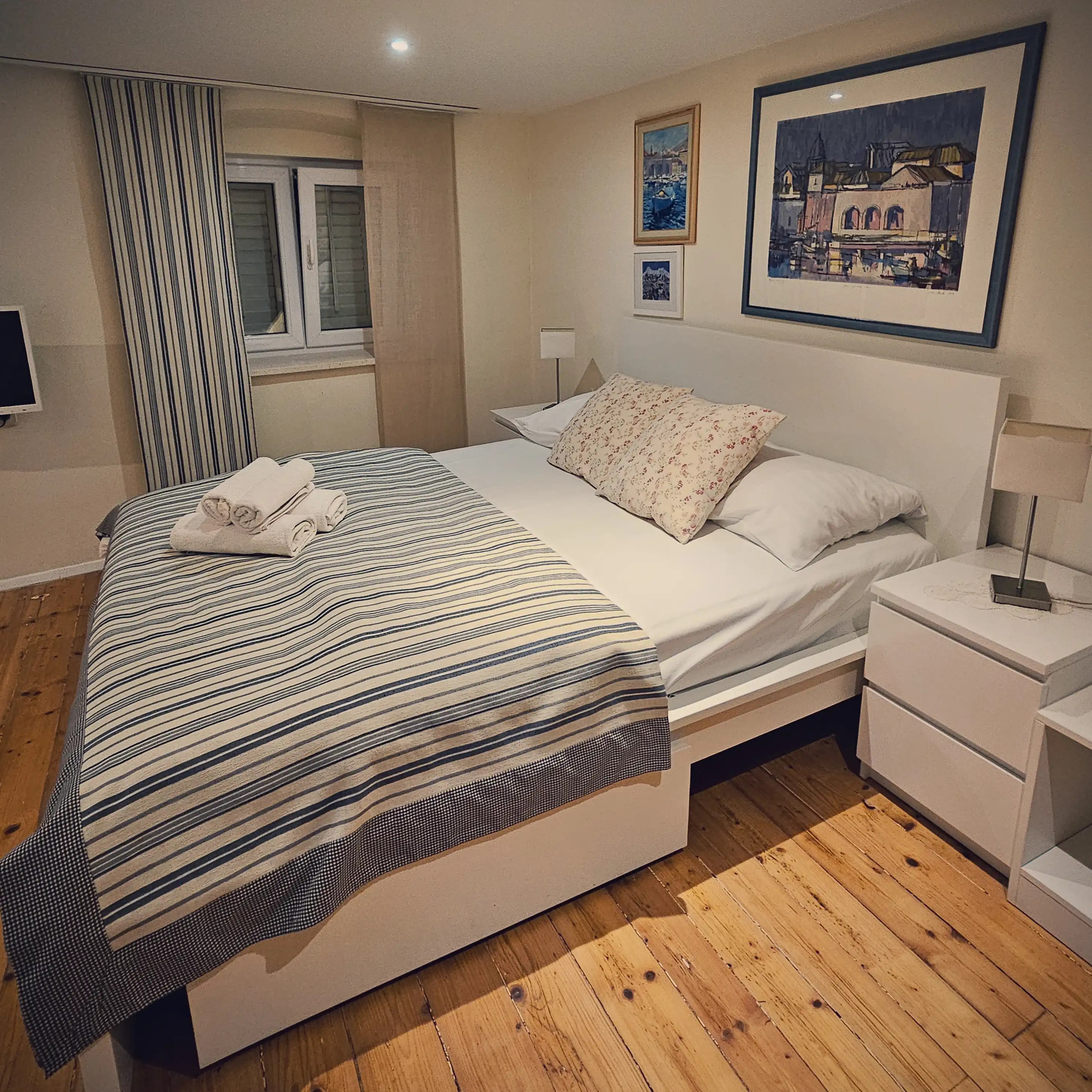 Cozy bedroom with striped linens and framed seaside artwork in a Dubrovnik apartment.