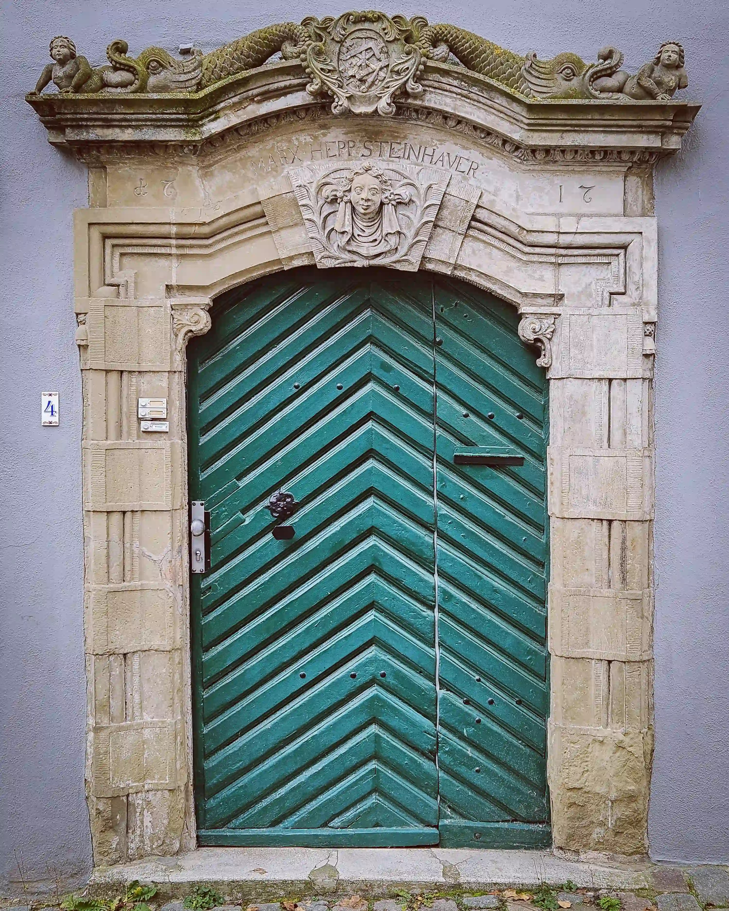 Green chevron-patterned wooden door framed by carved stone with figures and inscriptions in Herrenberg.
