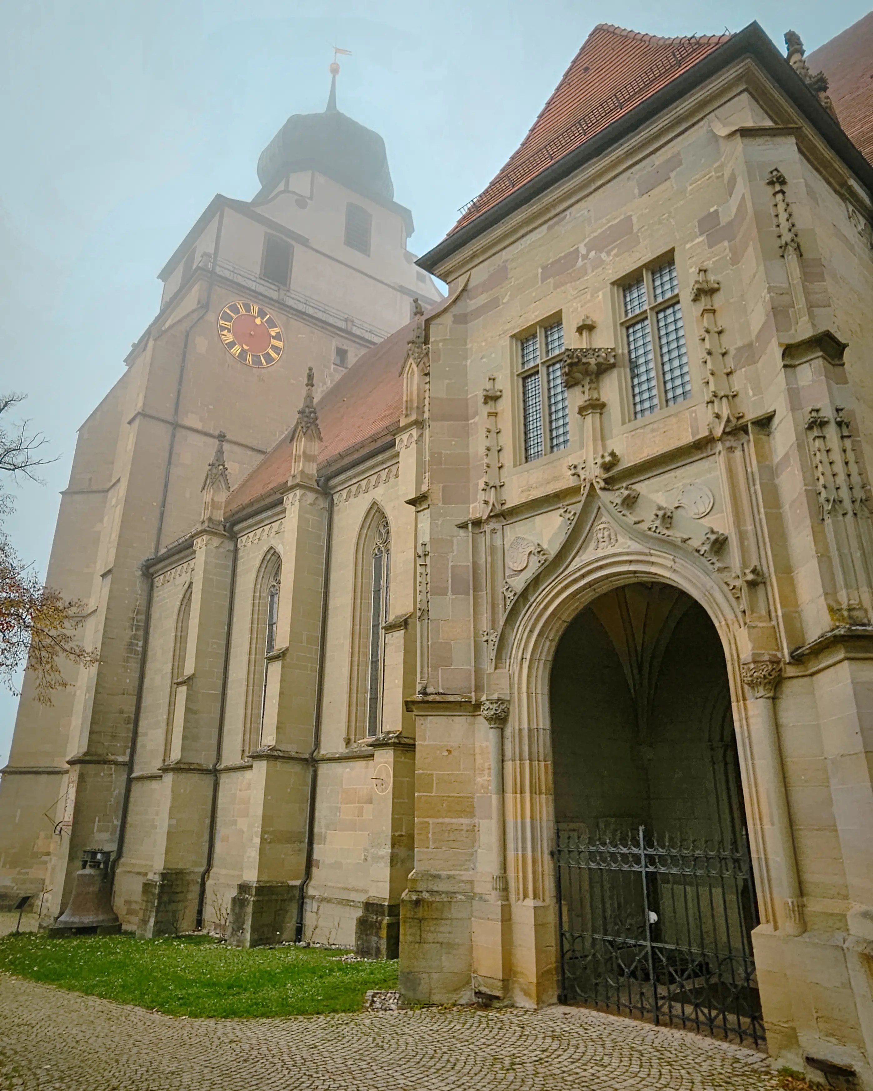 Exterior of the Stiftskirche Herrenberg with fog around its tower and Gothic entrance.
