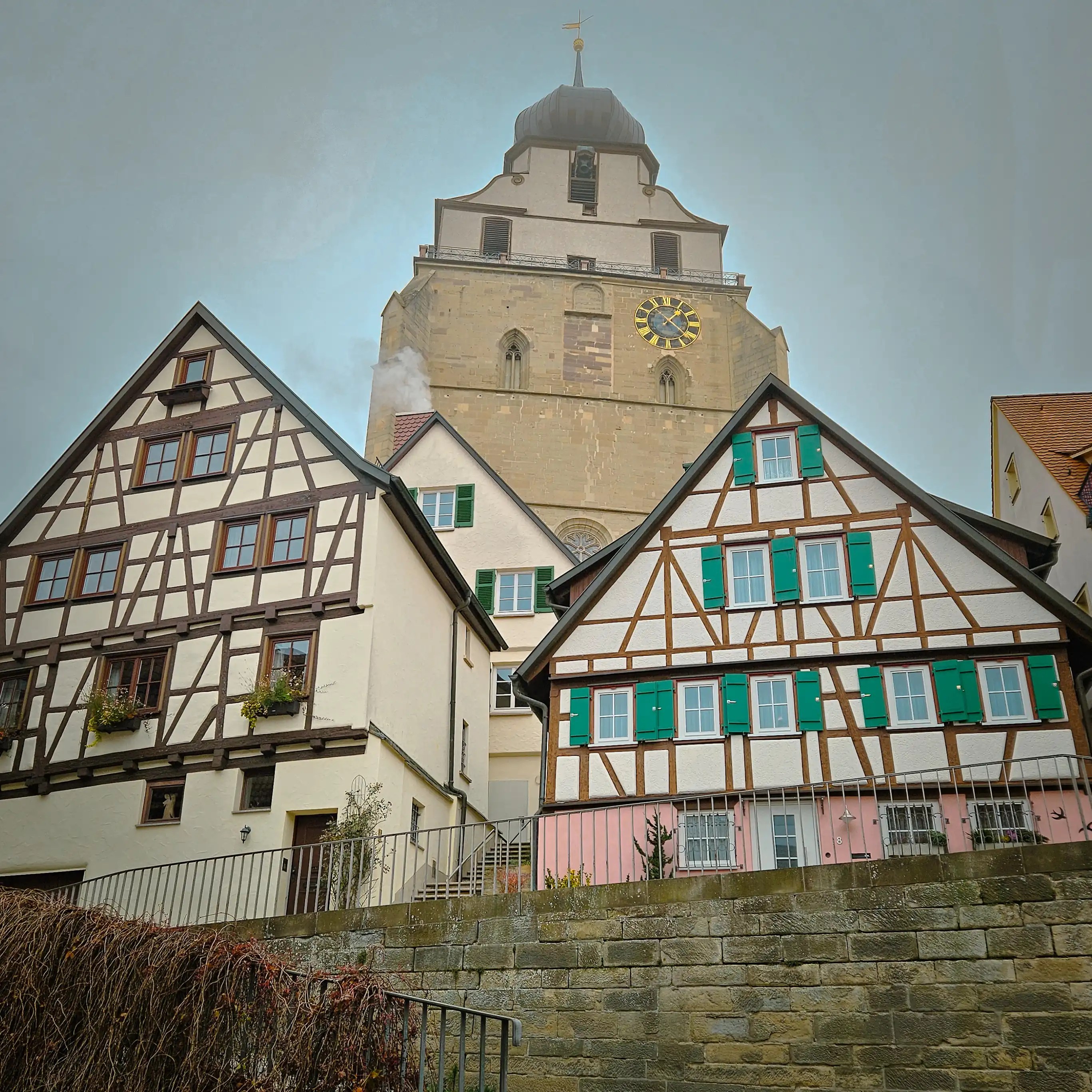 Half-timbered houses with green shutters below the Stiftskirche Herrenberg tower.