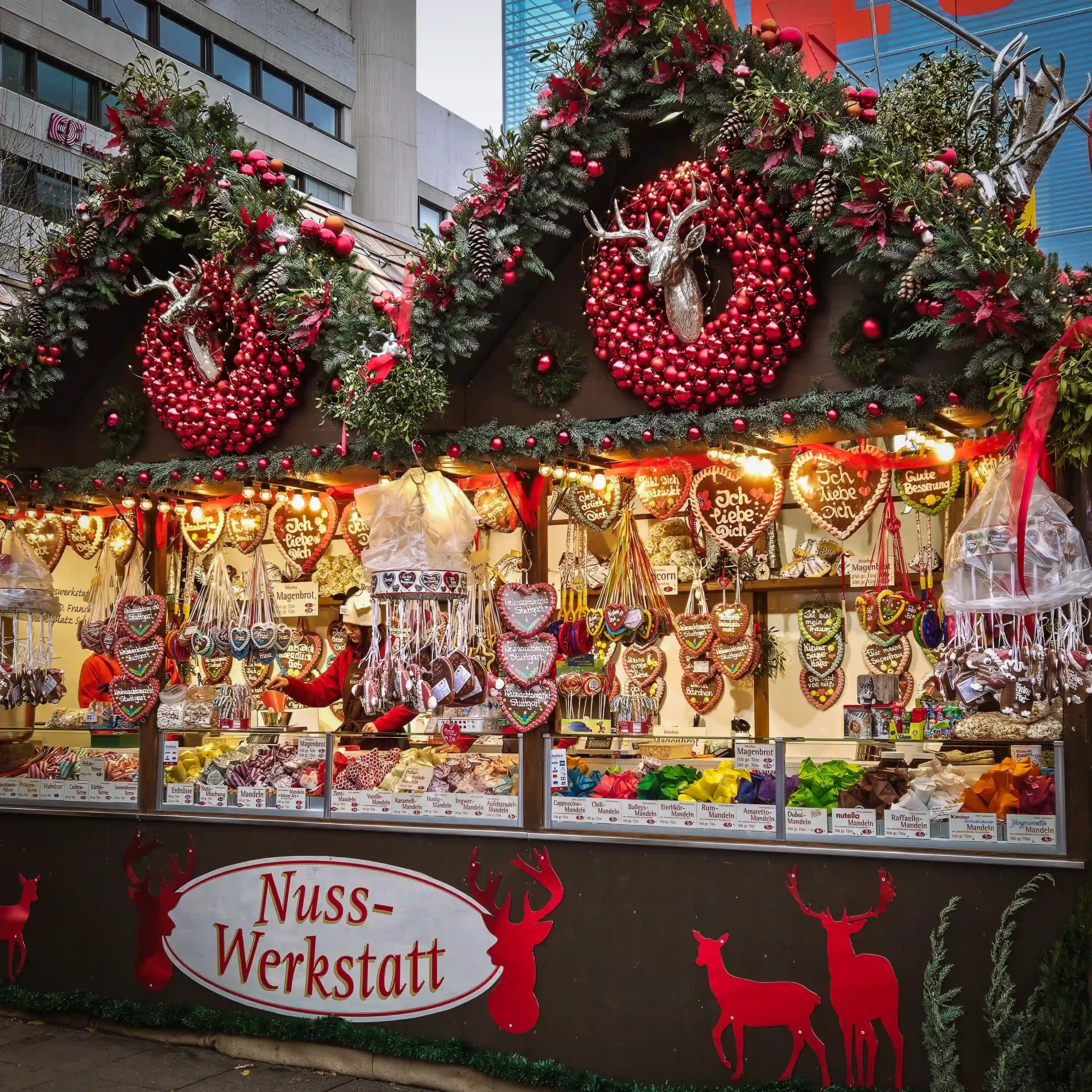Christmas market stall decorated with red wreaths and filled with gingerbread hearts, nuts, and sweets in Stuttgart.