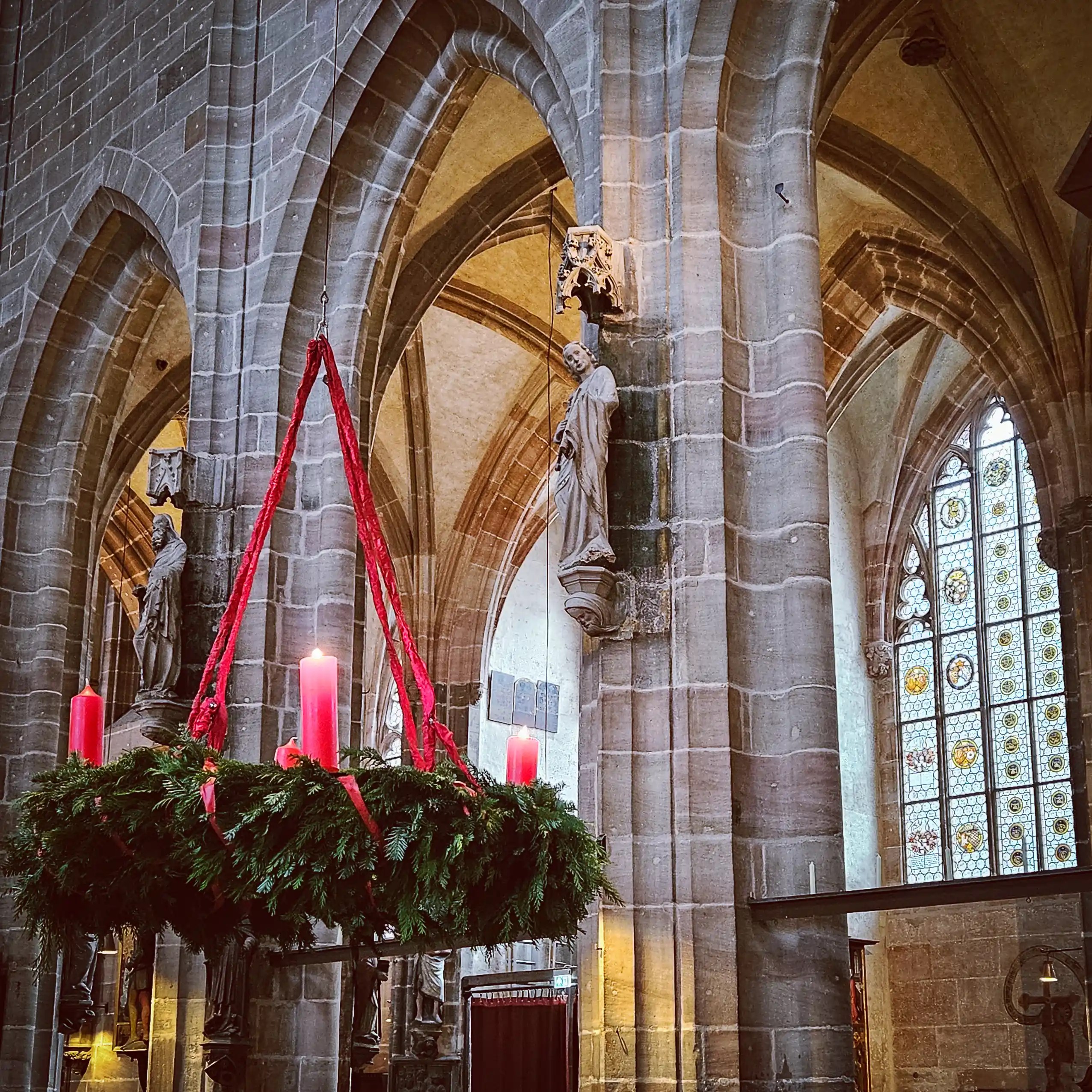 Large evergreen Advent wreath with four red candles hanging inside St. Lorenz Church in Nuremberg.