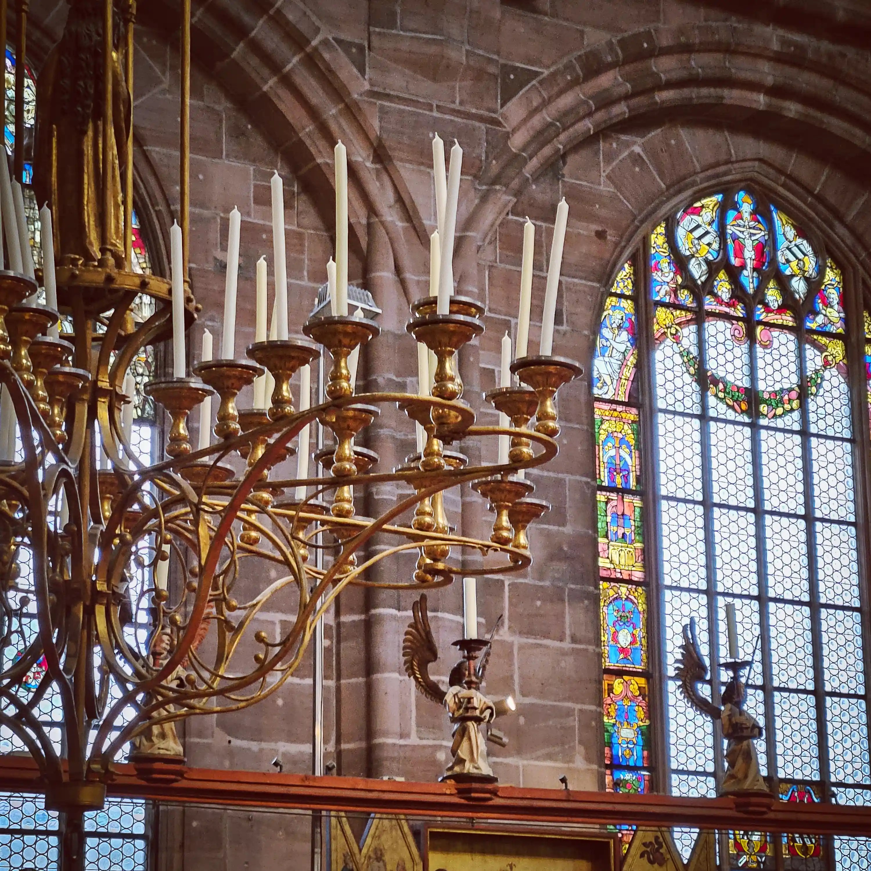 Golden candle chandelier and colorful stained glass windows inside St. Lorenz Church in Nuremberg.
