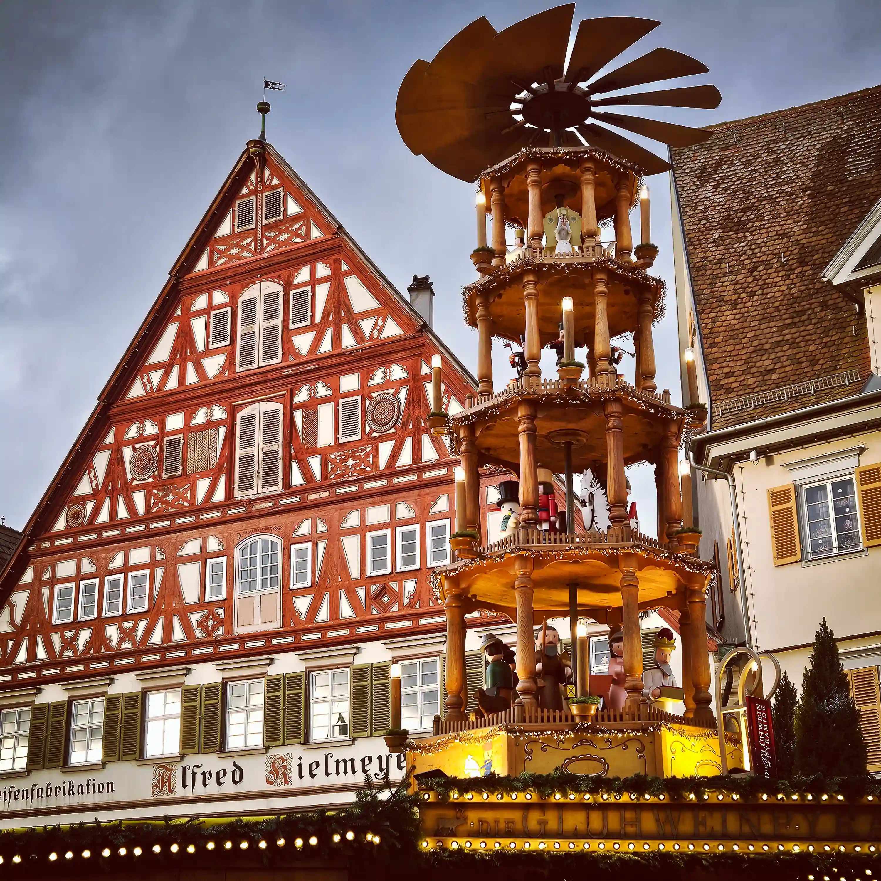 A tall wooden Christmas pyramid glowing beside Esslingen’s red half-timbered building at dusk.