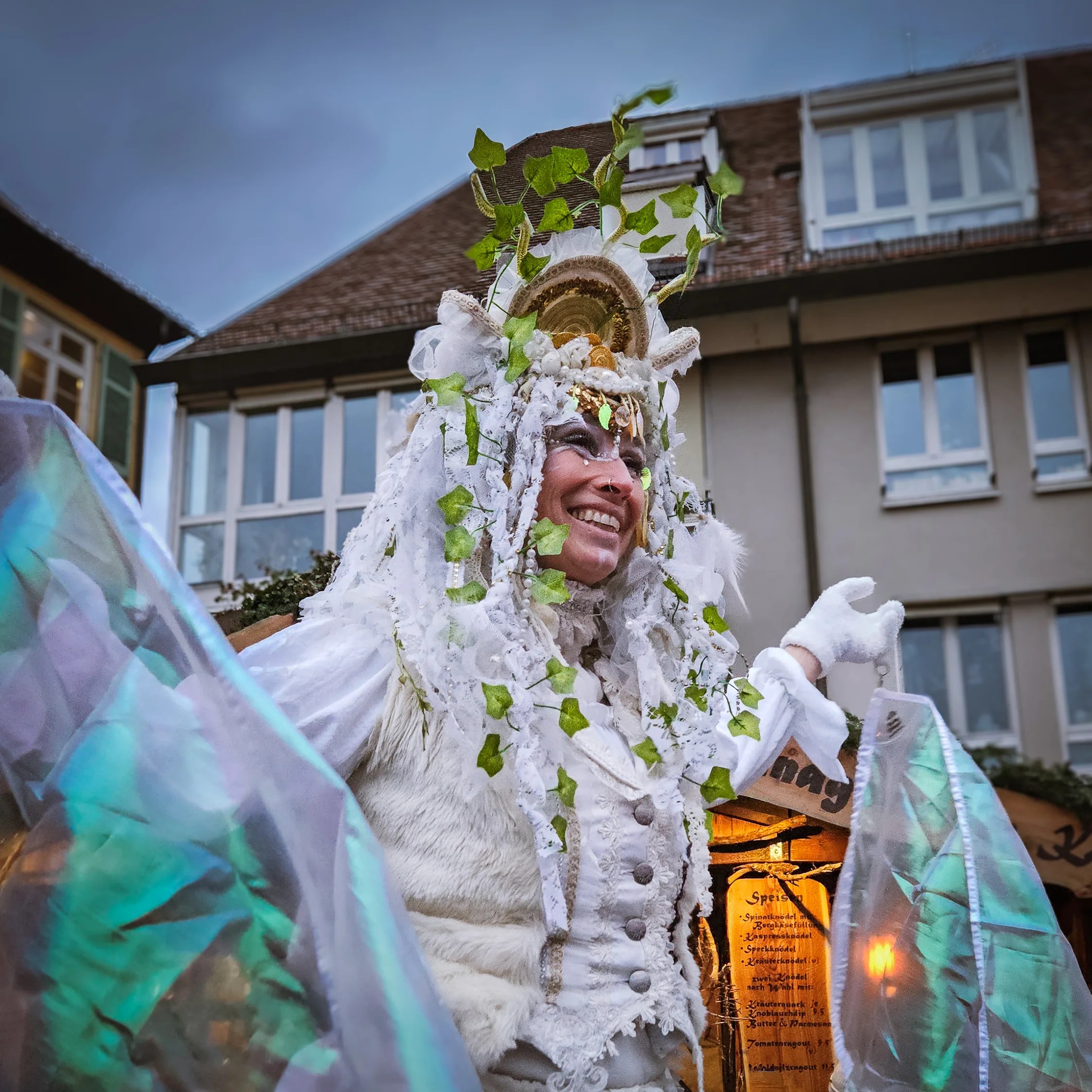 A smiling performer dressed in white and green ivy with glowing wings at the Esslingen Medieval Christmas Market.