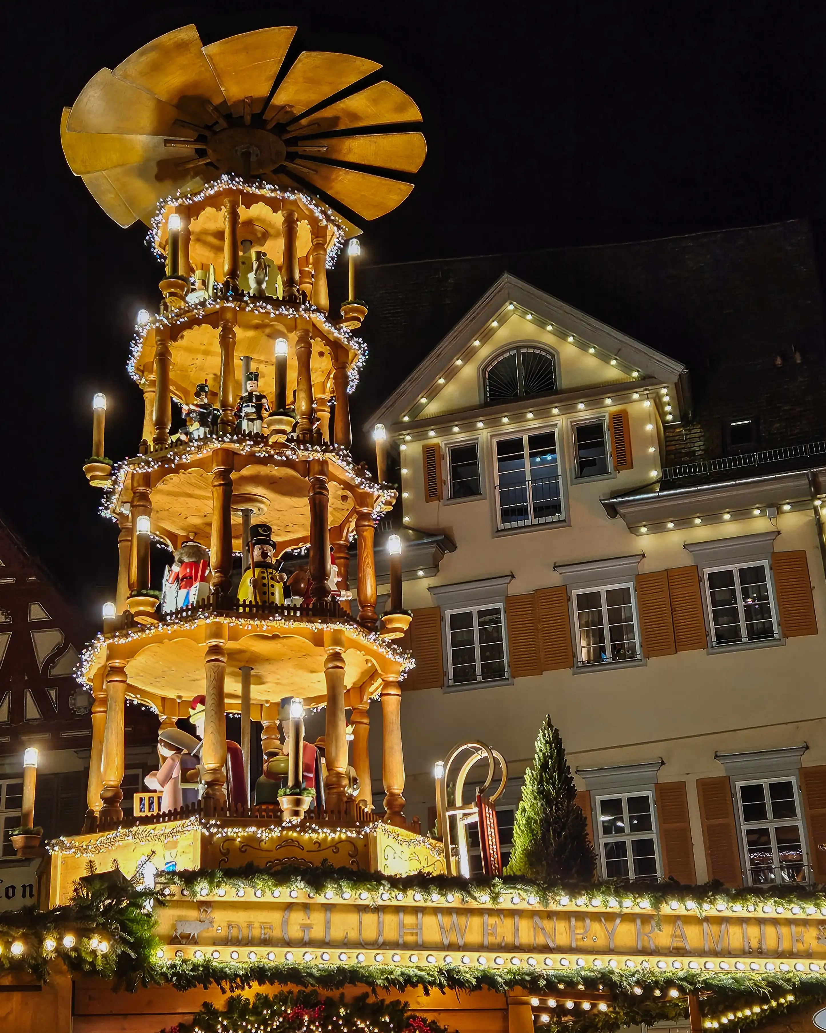 A tall illuminated wooden Christmas pyramid glowing with candlelight at the Esslingen Christmas Market at night.