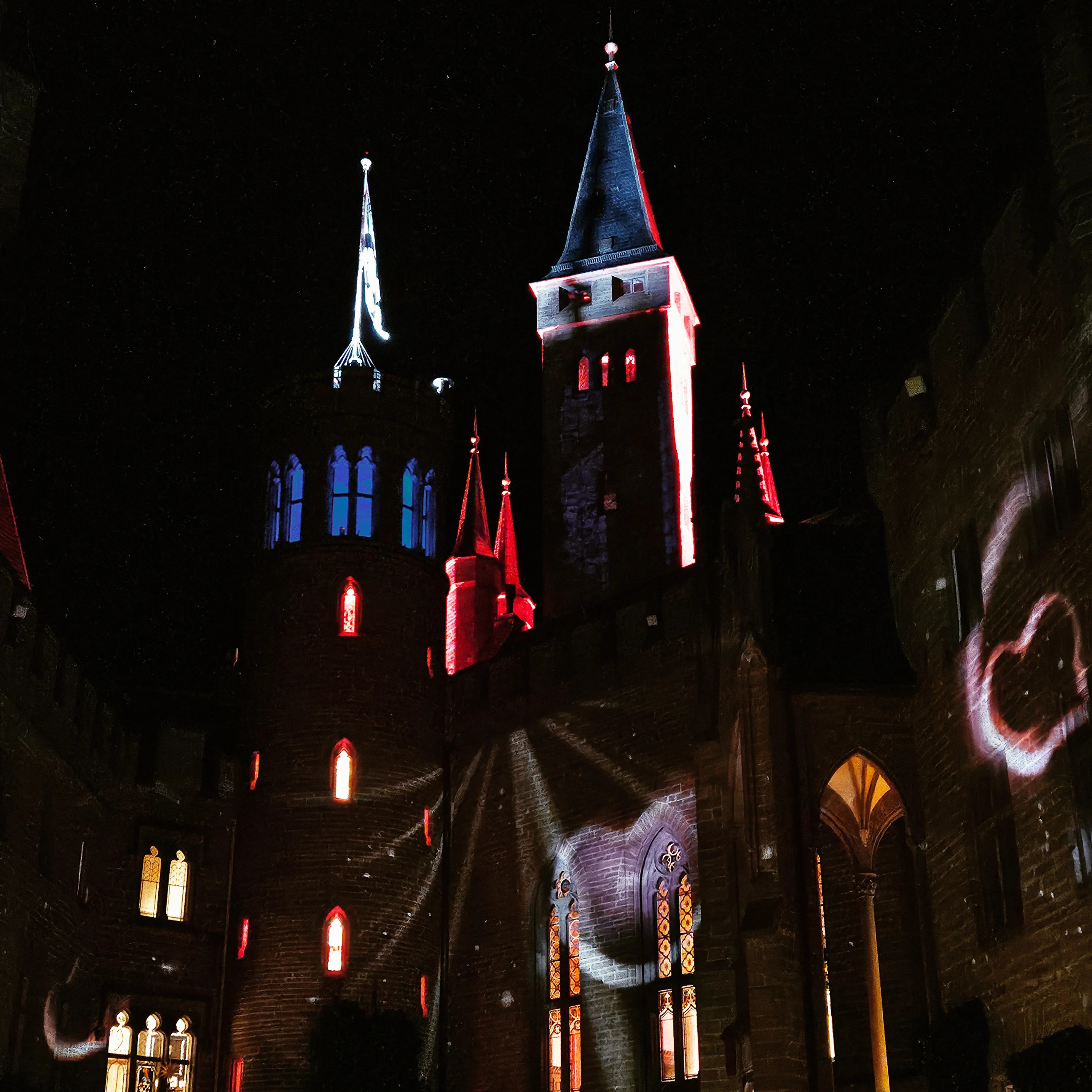 Night view of Burg Hohenzollern with colorful red and white light projections dancing across its towers.