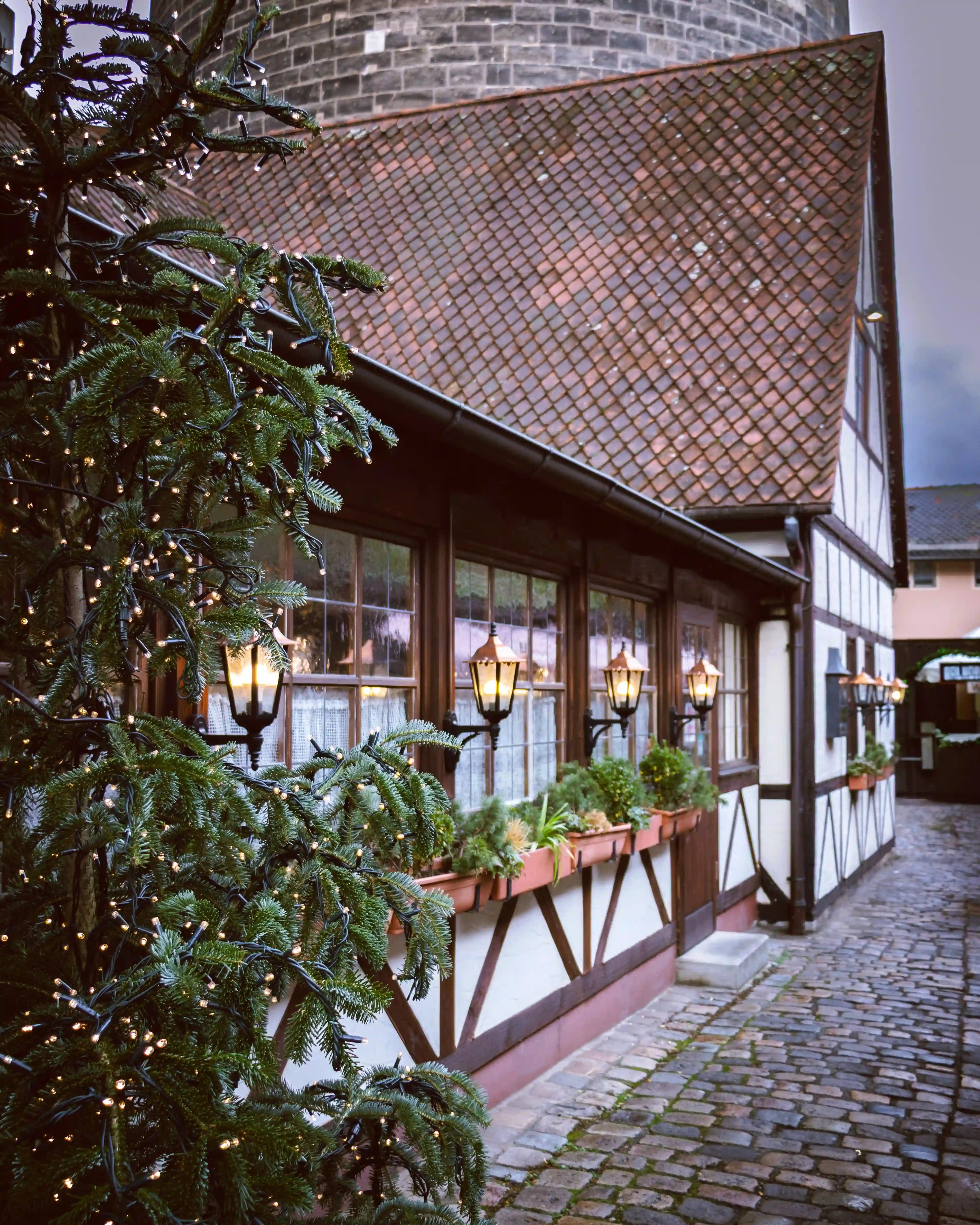 Narrow cobblestone lane lined with half-timbered buildings and Christmas greenery at the Handwerkerhof Nürnberg.