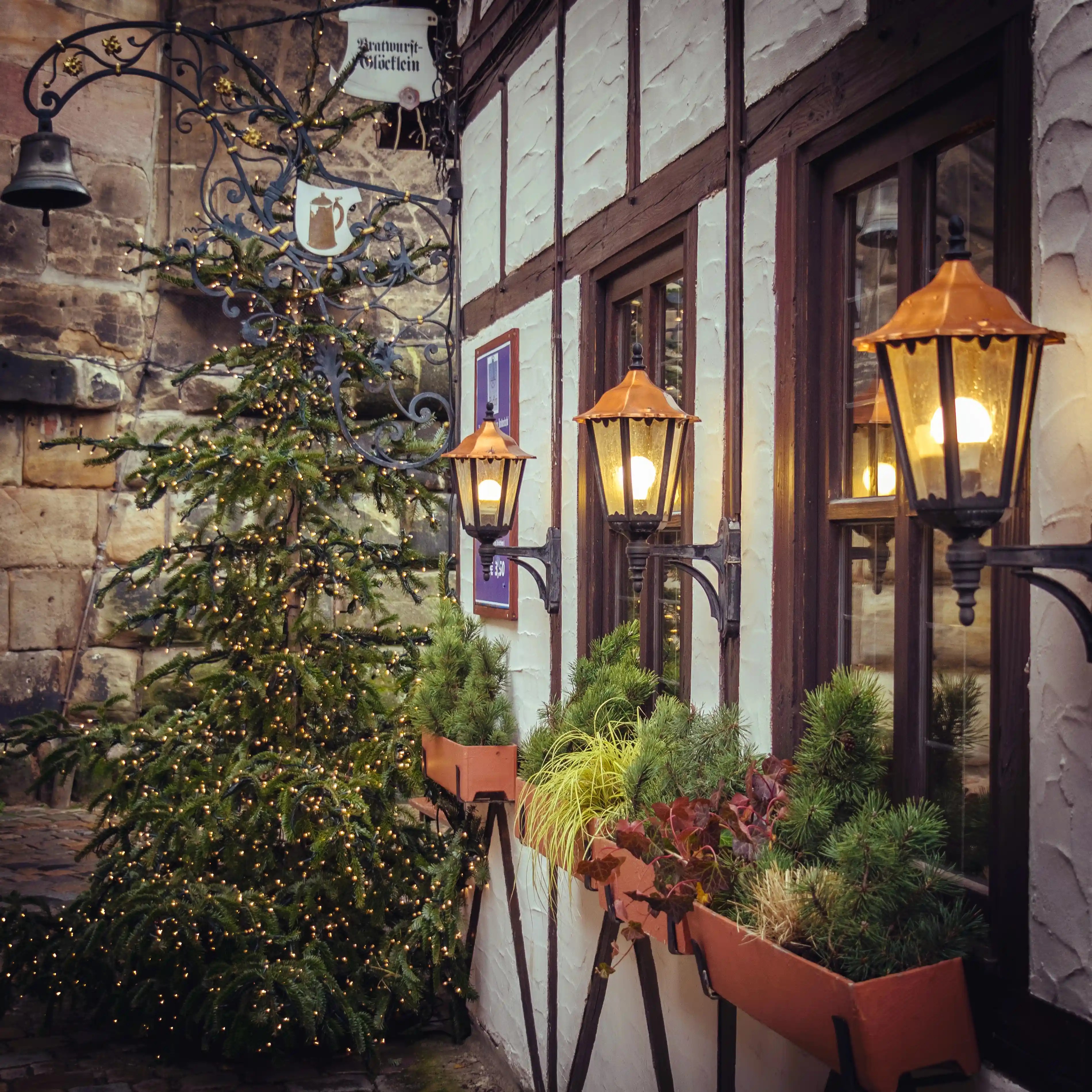 Christmas tree with twinkling lights beside old-fashioned lanterns and window boxes in Nuremberg’s Handwerkerhof.