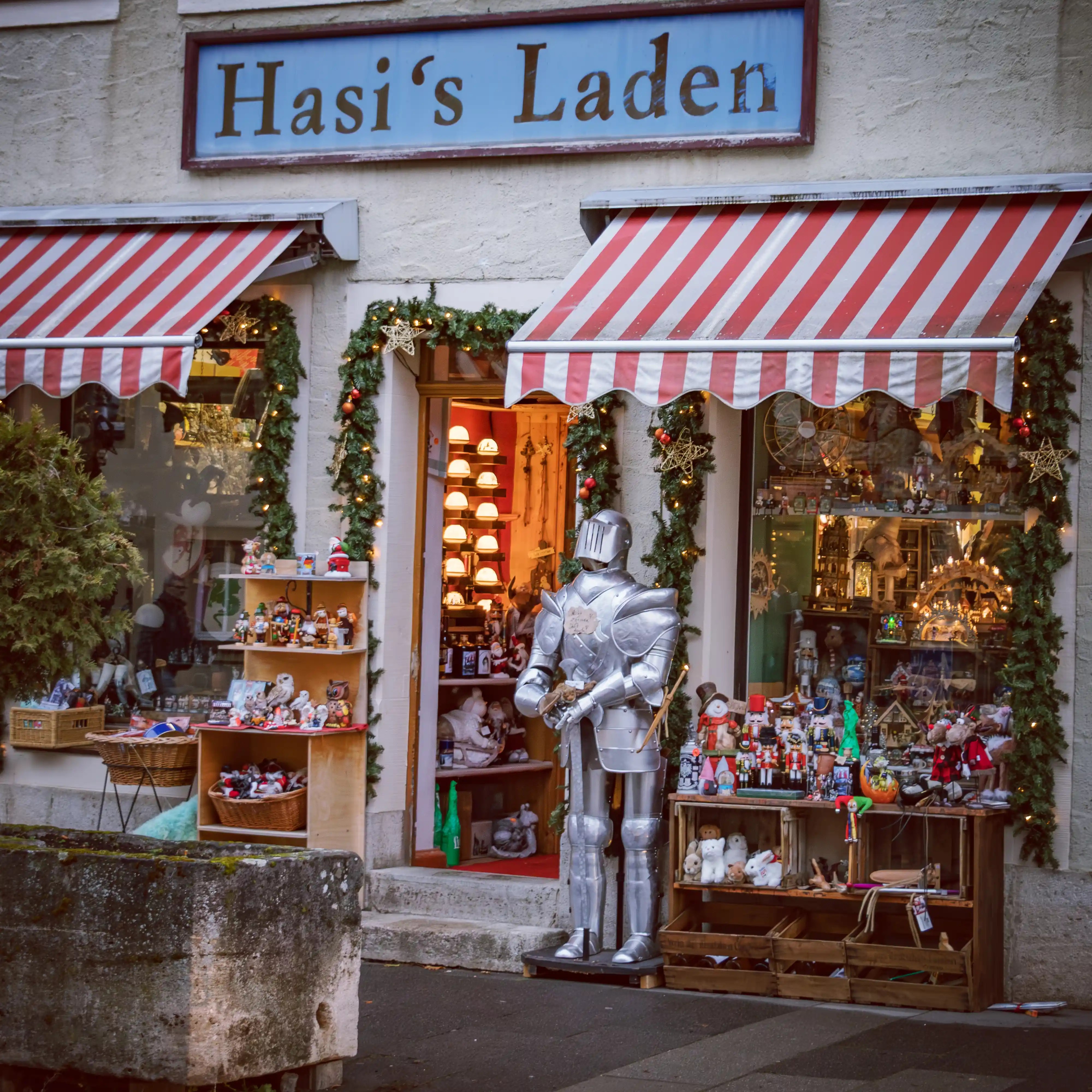 Festive shopfront of Hasi’s Laden in Rothenburg ob der Tauber with garlands, striped awnings, and a silver knight statue.