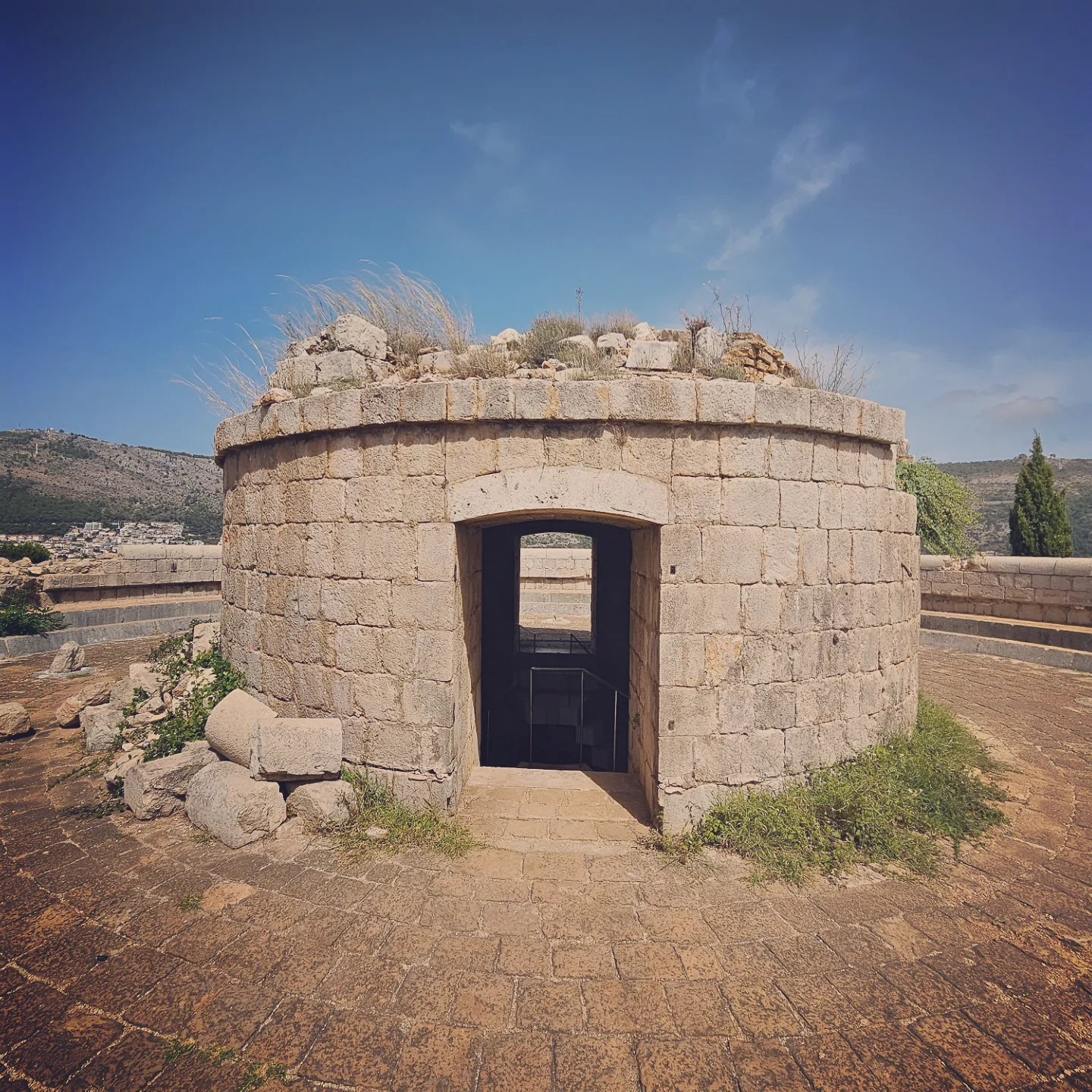 Stone entrance and circular outer wall of Fort Royal on Lokrum Island under a clear blue sky.
