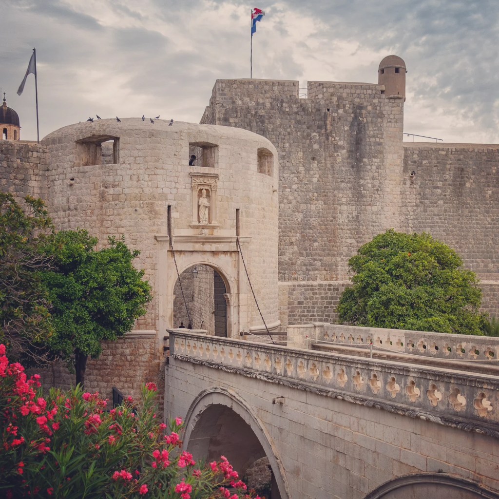 Pile Gate and stone bridge leading into Dubrovnik’s Old Town with Croatian flag flying above.