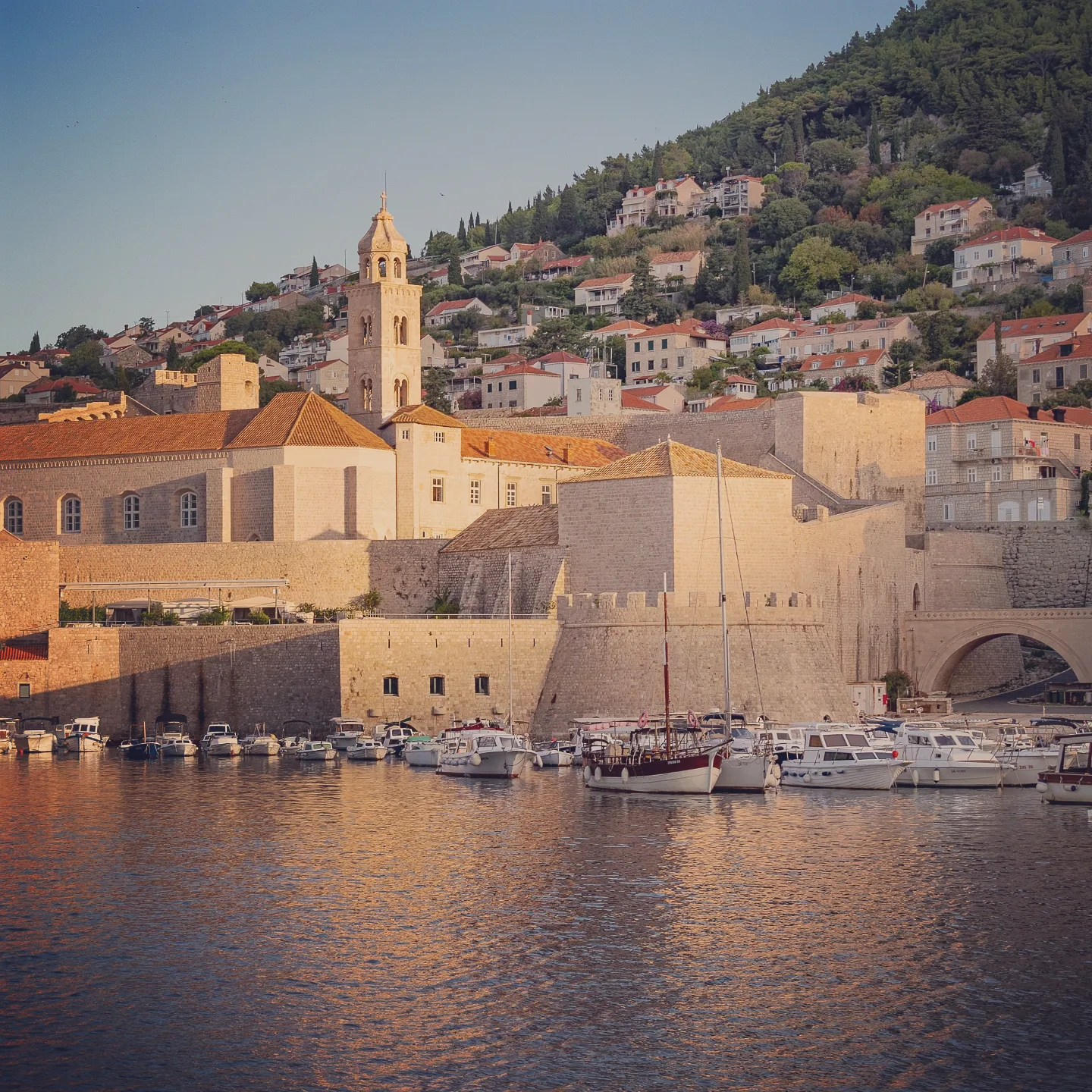 Boats moored in Dubrovnik’s Old Port at sunset with the Dominican Monastery in the background.