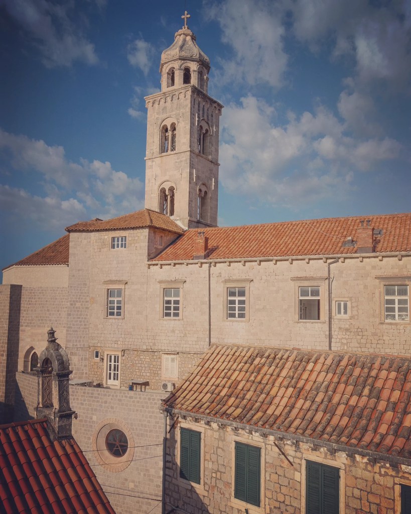 Dominican Monastery bell tower in Dubrovnik with red rooftops and blue sky.