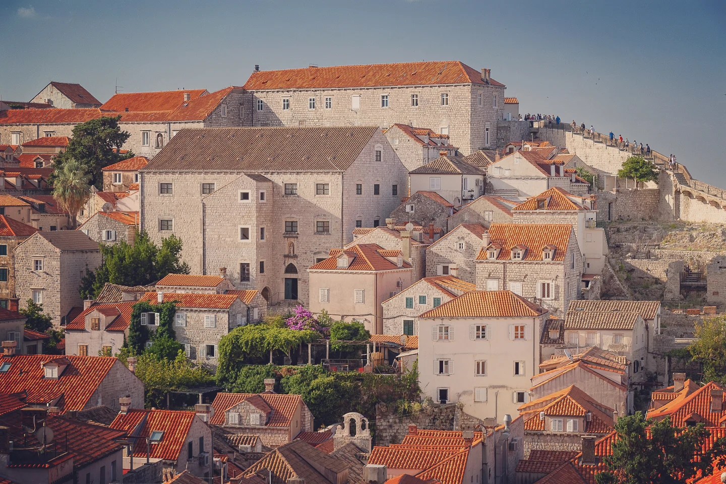 Stone houses and sections of Dubrovnik’s city walls with red rooftops and summer greenery.