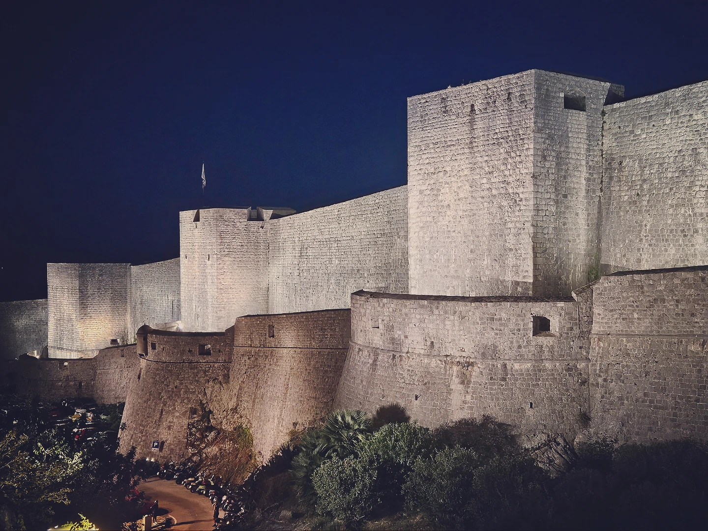 Illuminated stone city walls of Dubrovnik glowing against the deep blue night sky.