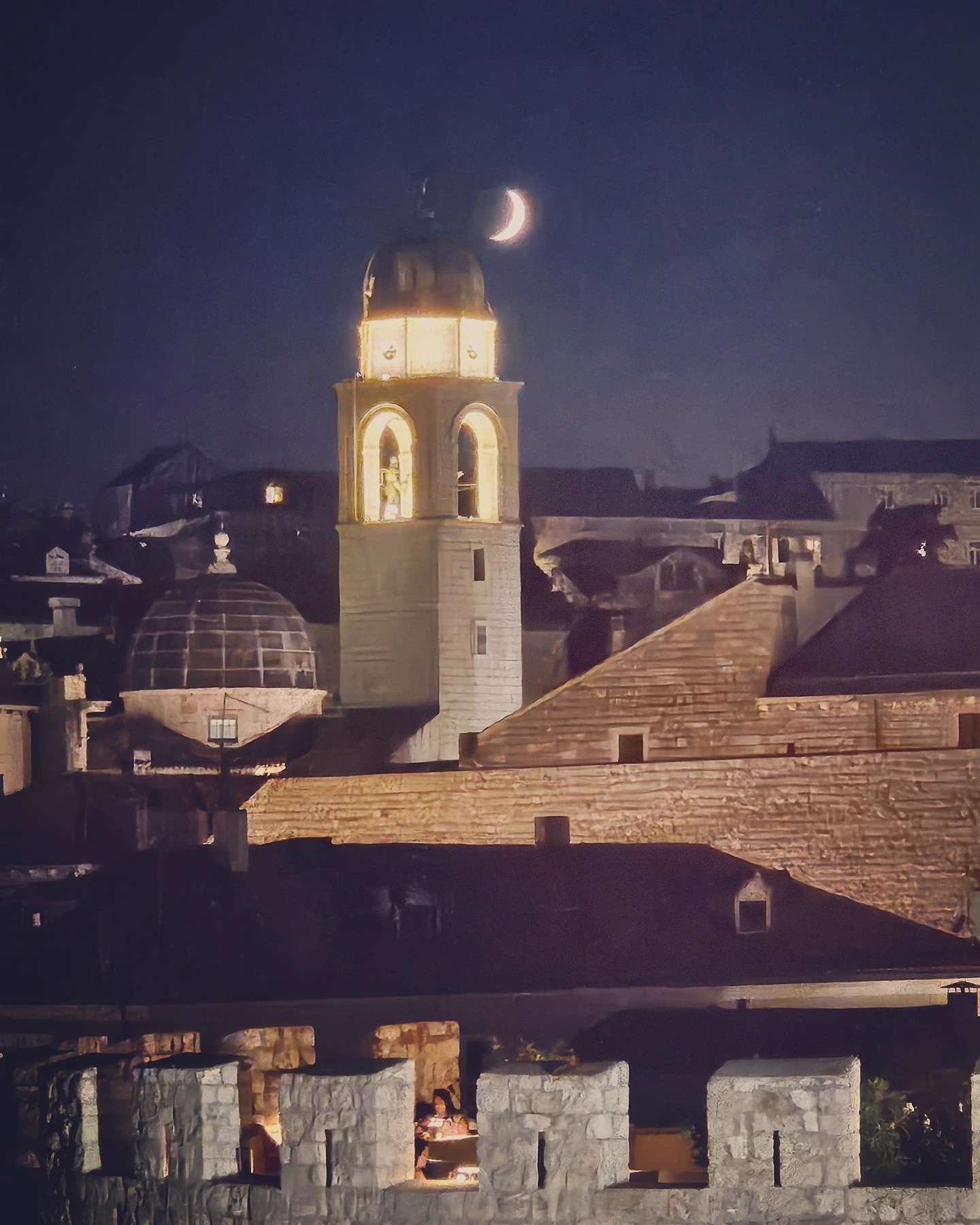 Crescent moon hanging over the illuminated bell tower of Dubrovnik’s Old Town at night.