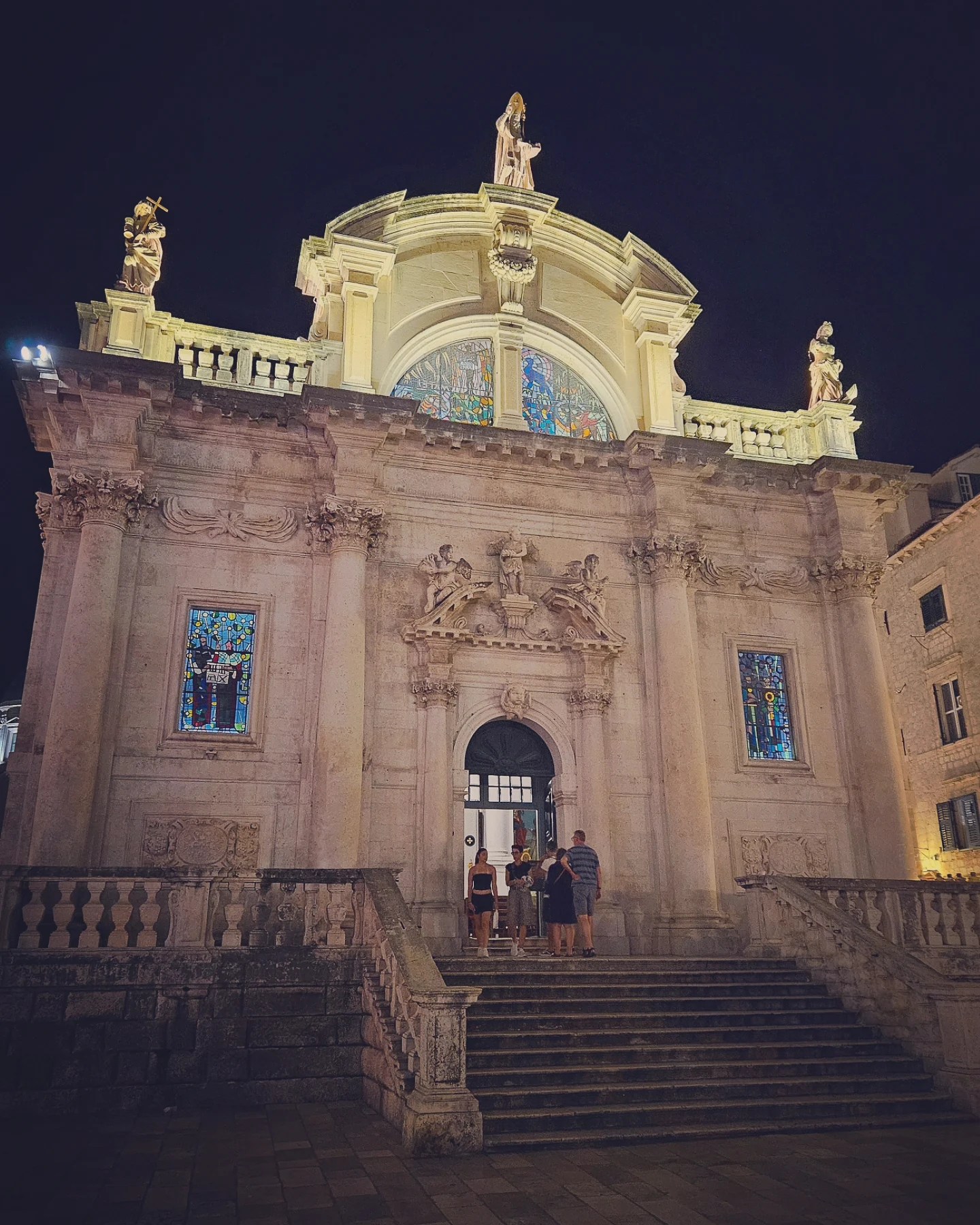 St. Blaise Church in Dubrovnik’s Old Town illuminated at night with visitors on the steps.