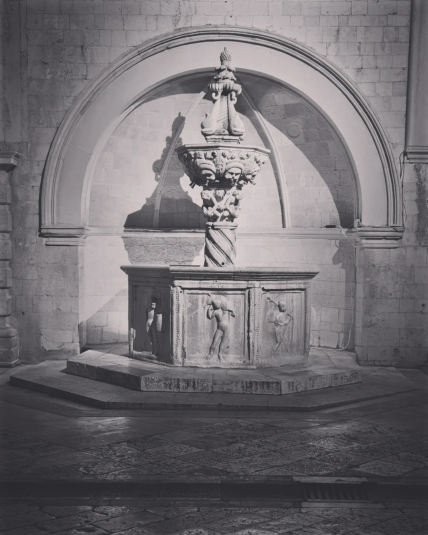 Ornate stone fountain in black and white, showing carved figures and arches in Dubrovnik’s Old Town.