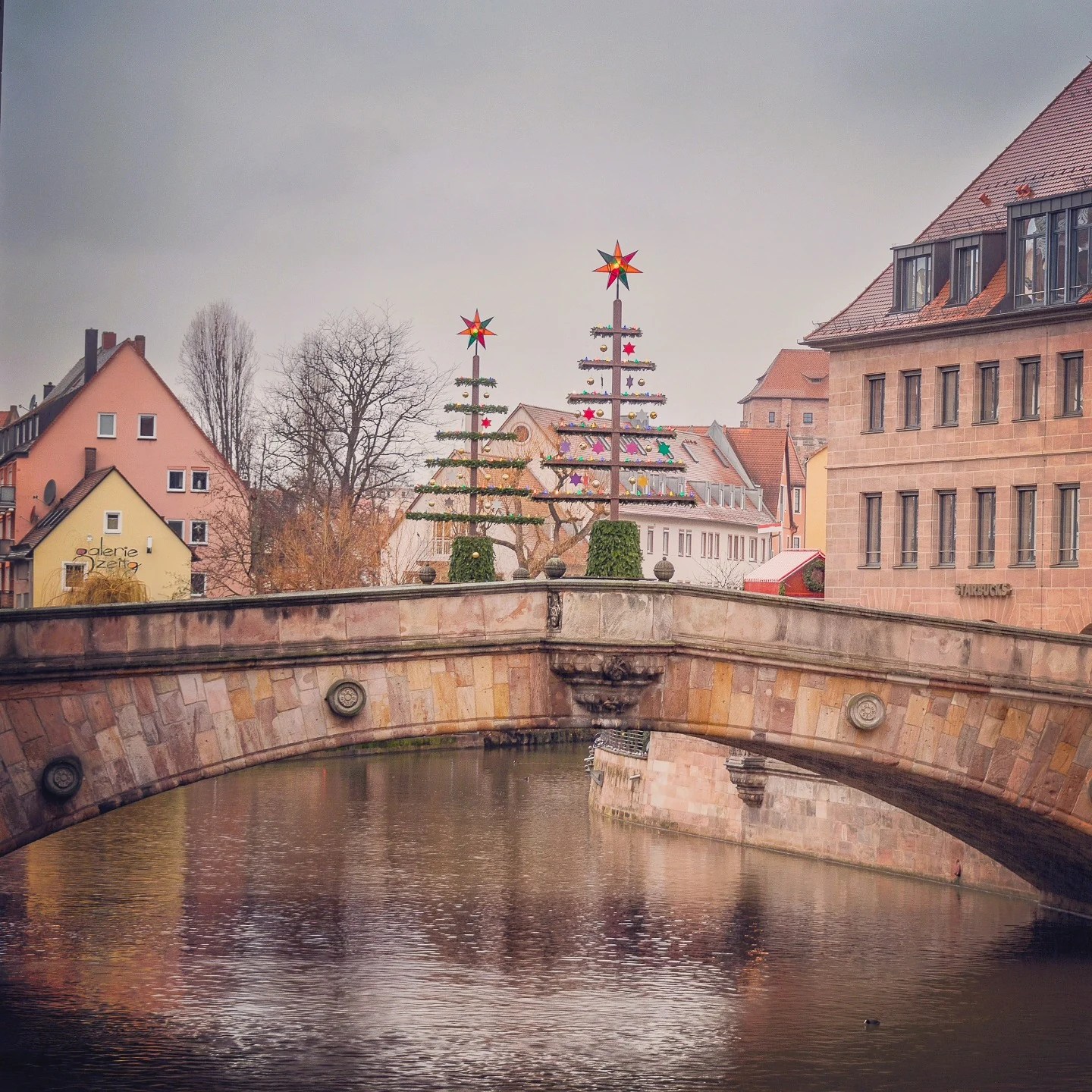 Stone bridge over the Pegnitz River in Nuremberg decorated with modern Christmas tree sculptures and stars.