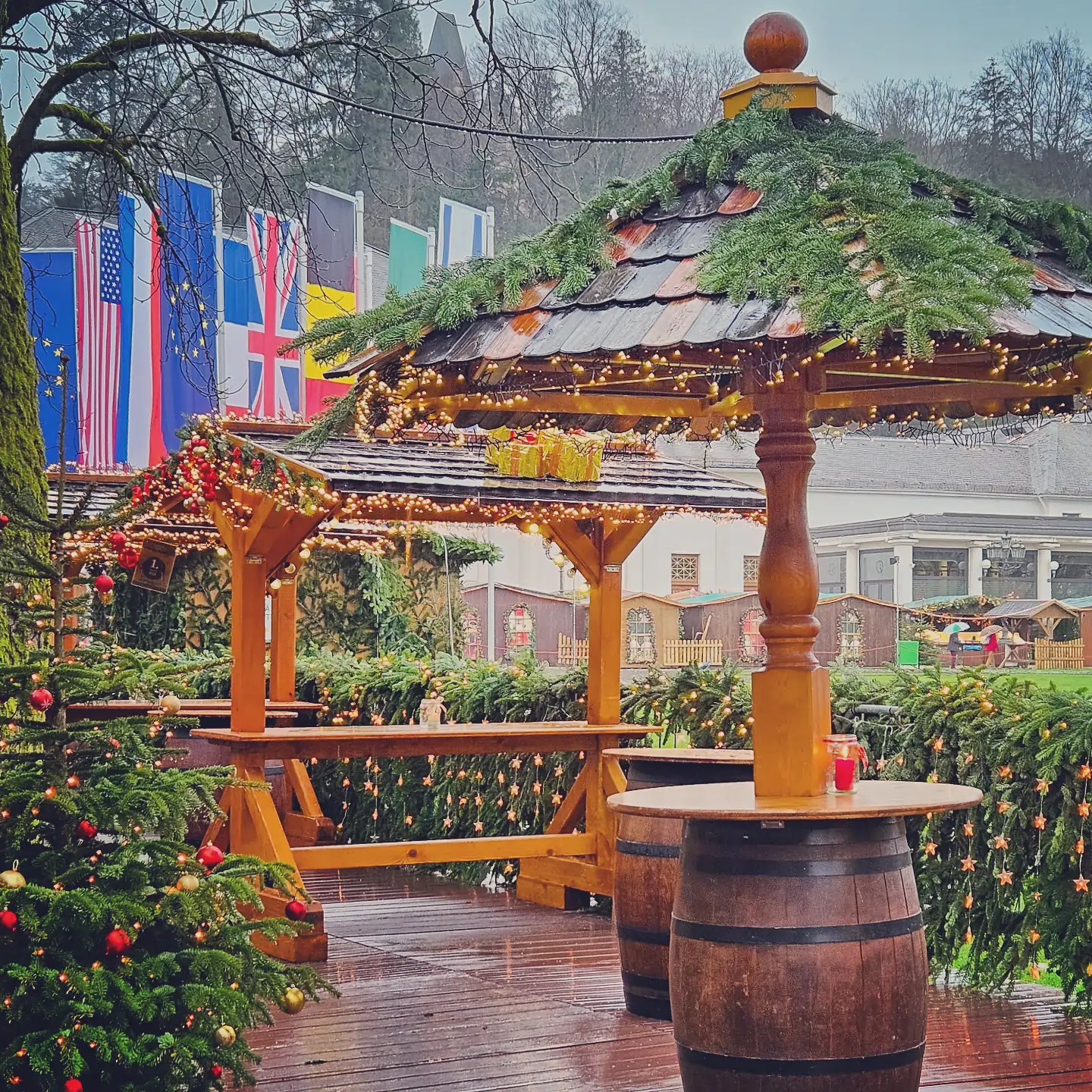 Wooden market huts decorated with lights and garlands, with international flags in the background at the Baden-Baden Christmas Market.