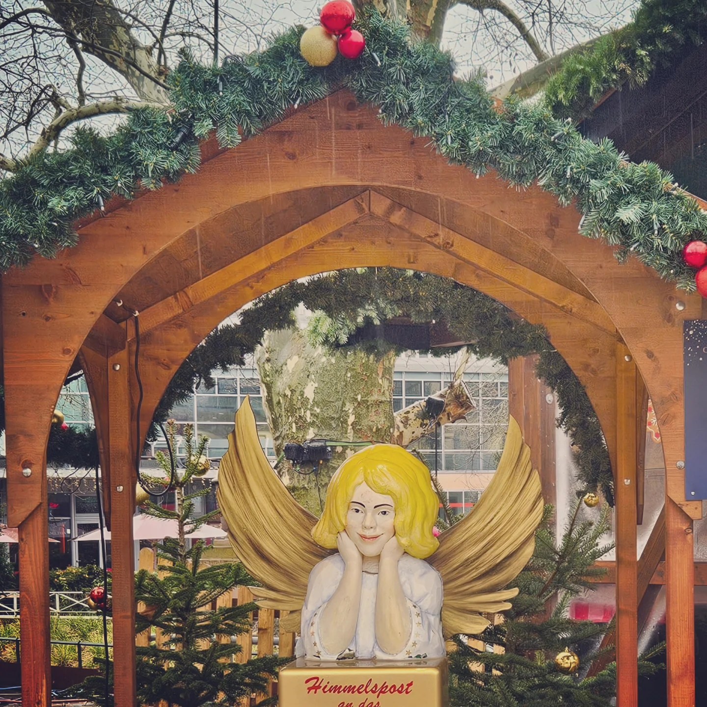 Angel mailbox labeled “Himmelspost” surrounded by small fir trees and holiday decorations.