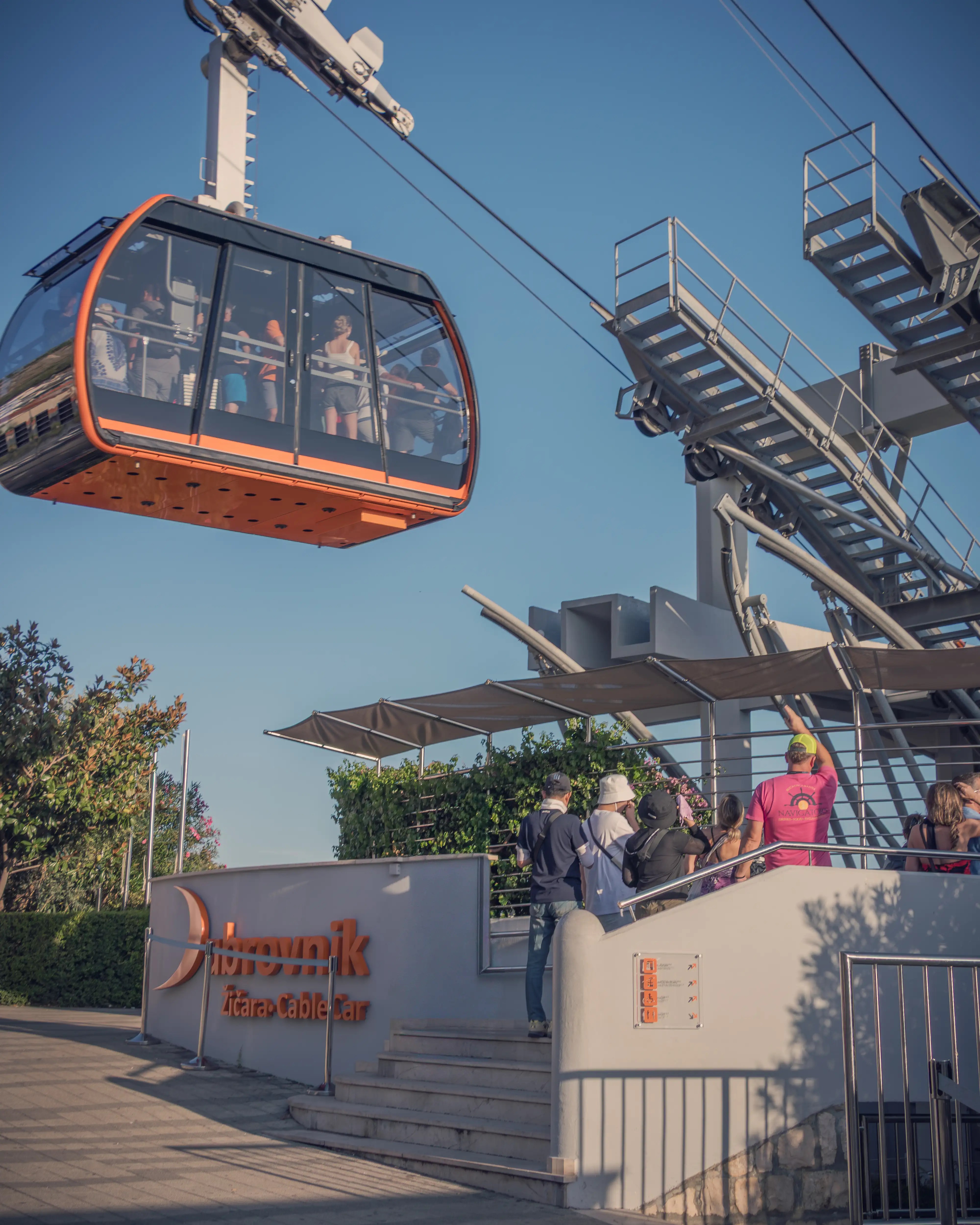 Orange cable car departing the Dubrovnik station on a clear afternoon.