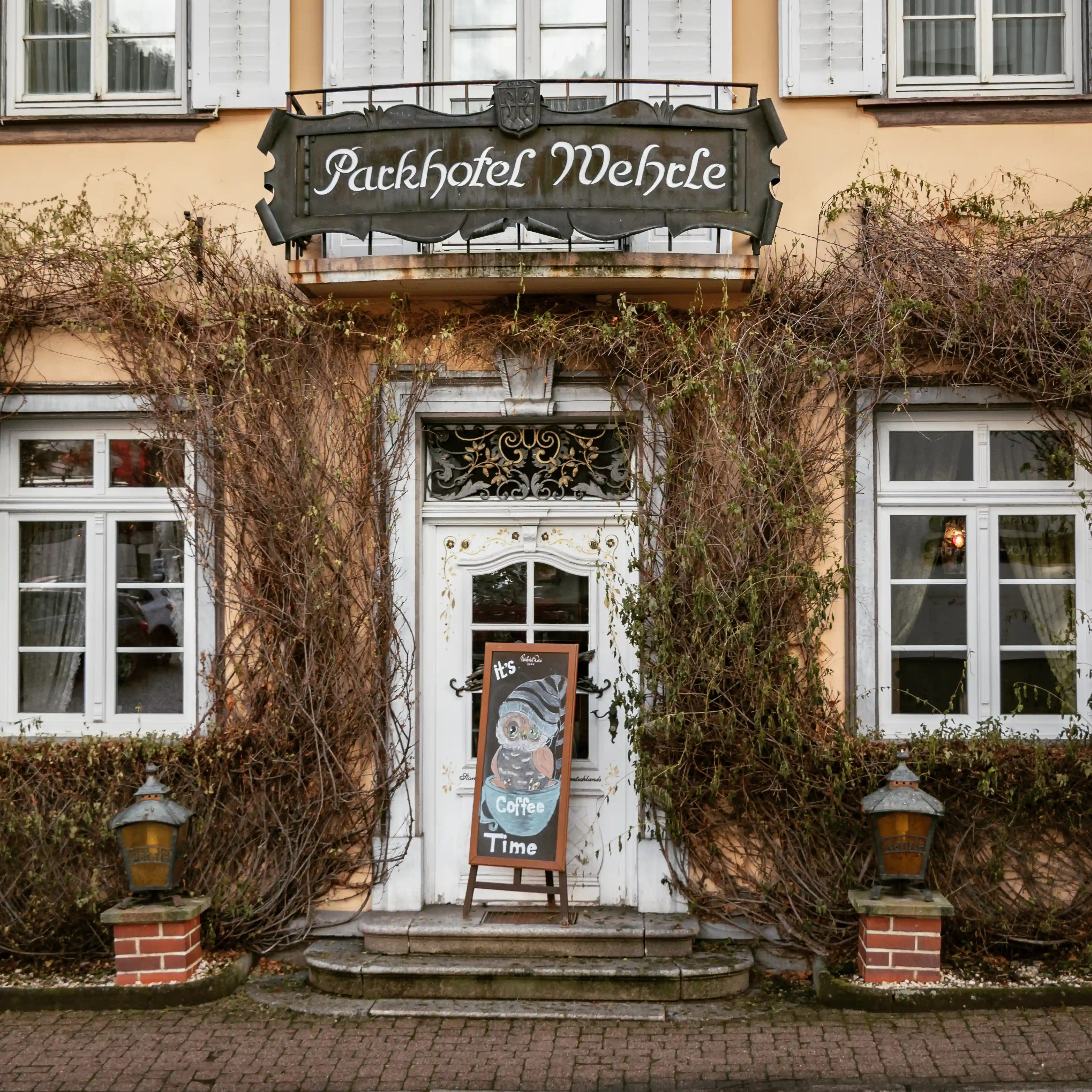 Historic entrance of Parkhotel Wehrle in Triberg with ivy-covered walls and a chalkboard sign reading “It’s Coffee Time.”