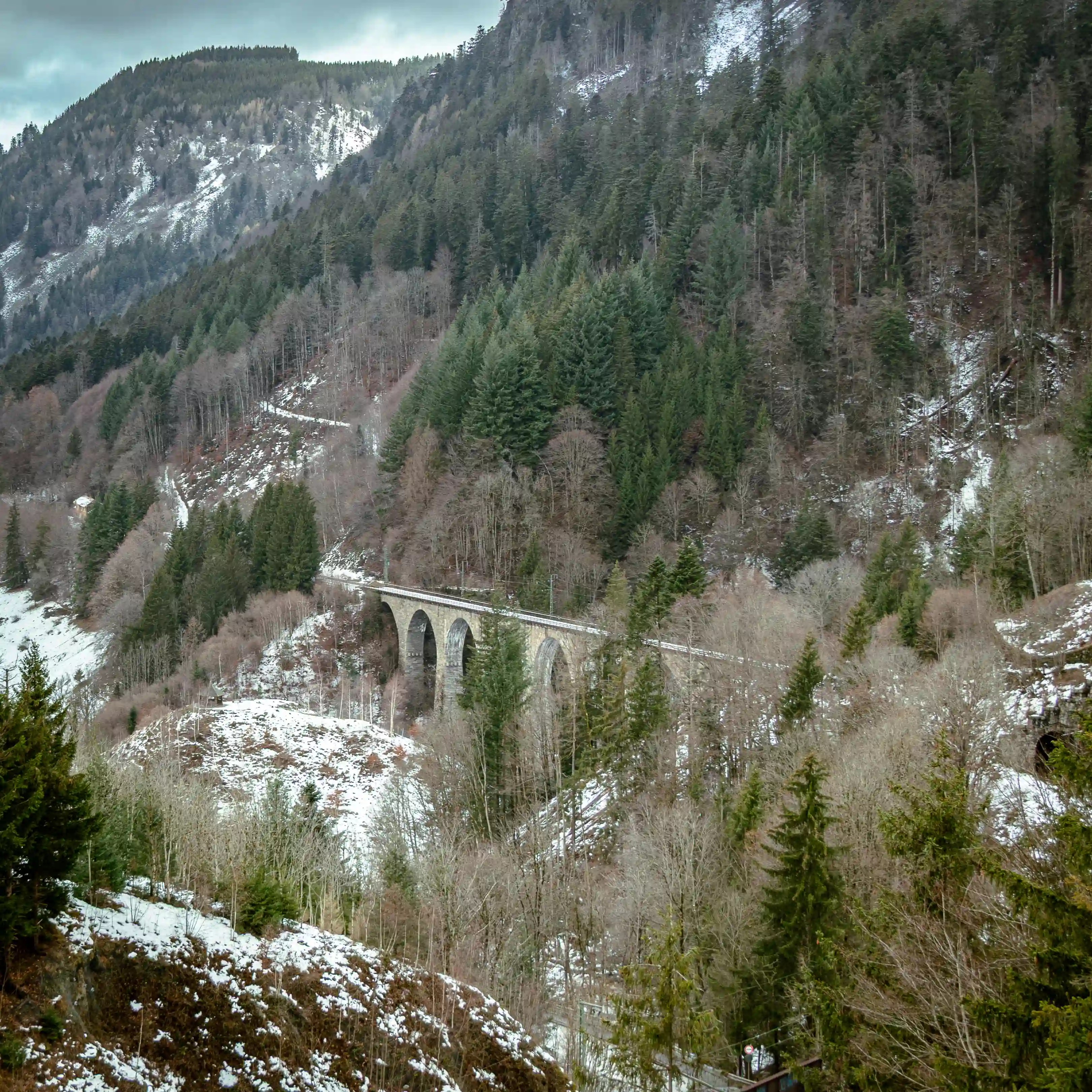 Distant view of the Ravenna Viaduct crossing a snow-dusted Black Forest hillside surrounded by pine trees.