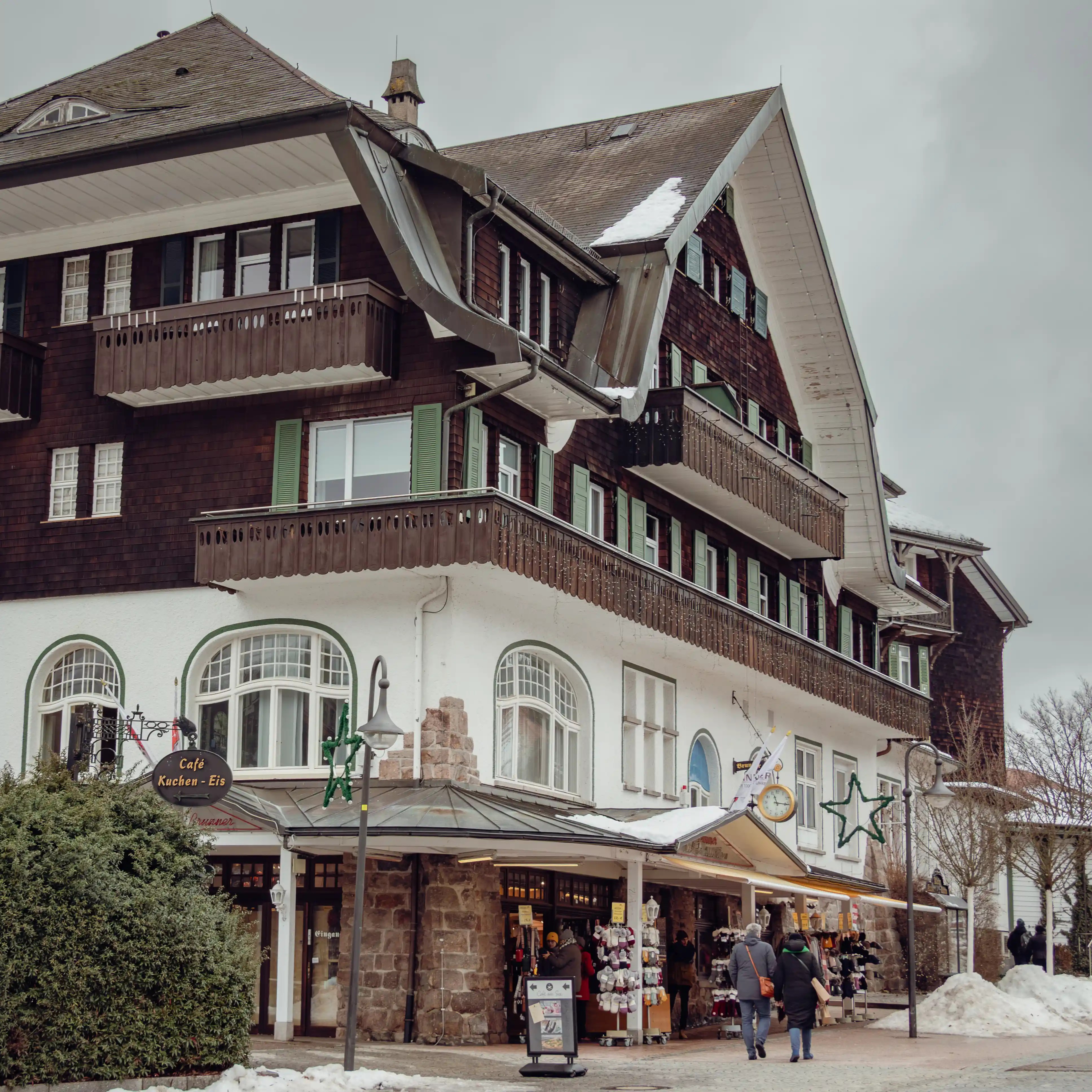 Shoppers walking along a snow-lined street with alpine-style buildings and stores in Titisee, Germany.