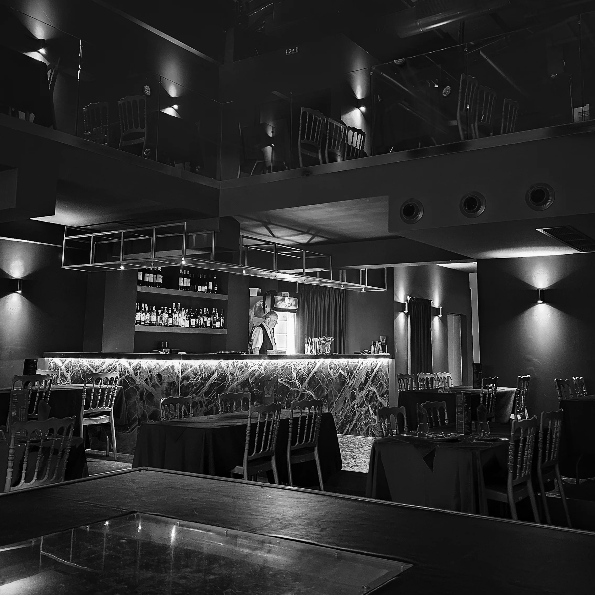 Black-and-white photo of the Troy Dinner Show bar area with illuminated marble counter and empty tables.