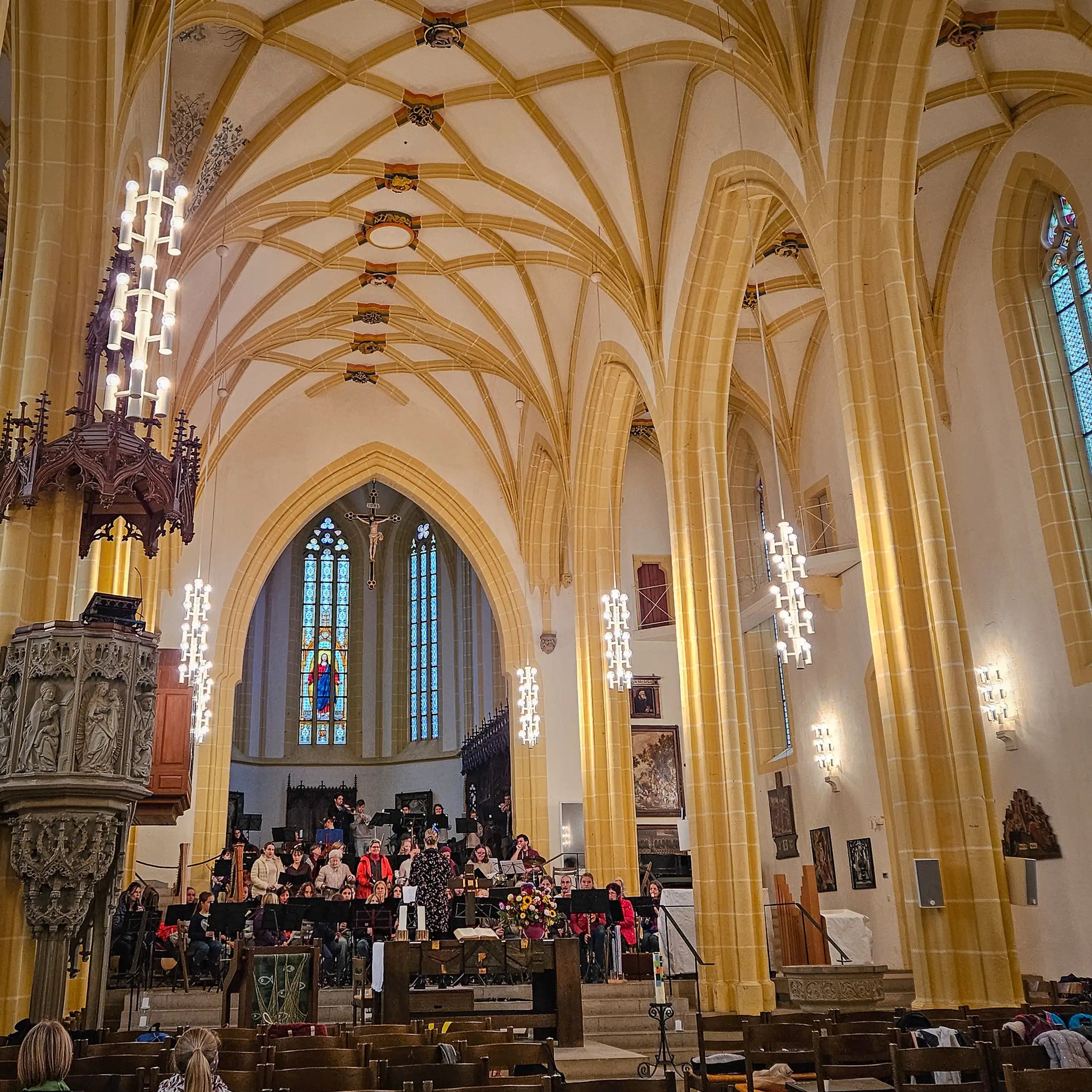 Interior of Stiftskirche Herrenberg with vaulted Gothic ceiling, chandeliers, and a choir performing near the altar.