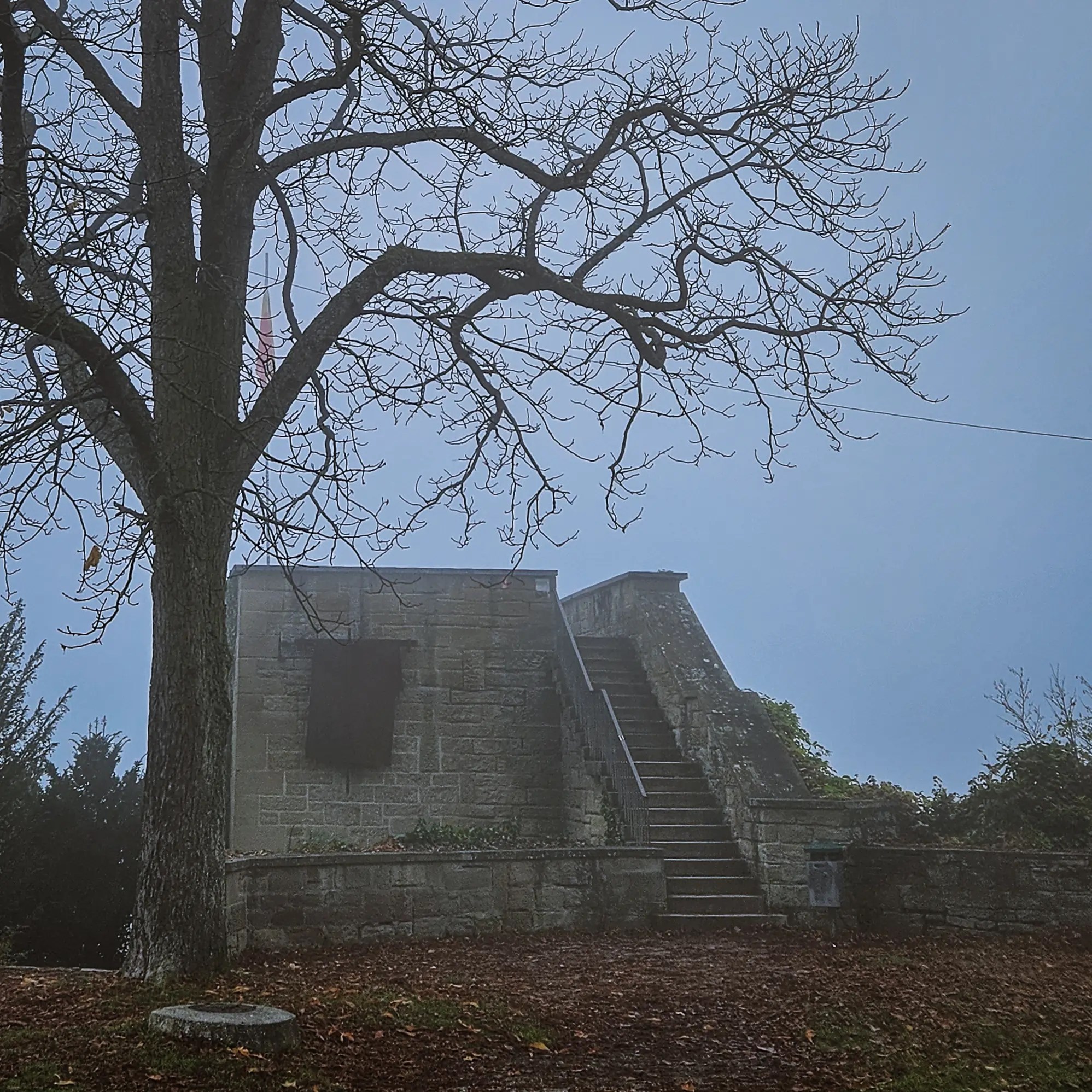 Stone platform of the Pulverturm on Herrenberg’s Schlossberg surrounded by fog and bare trees in late autumn.