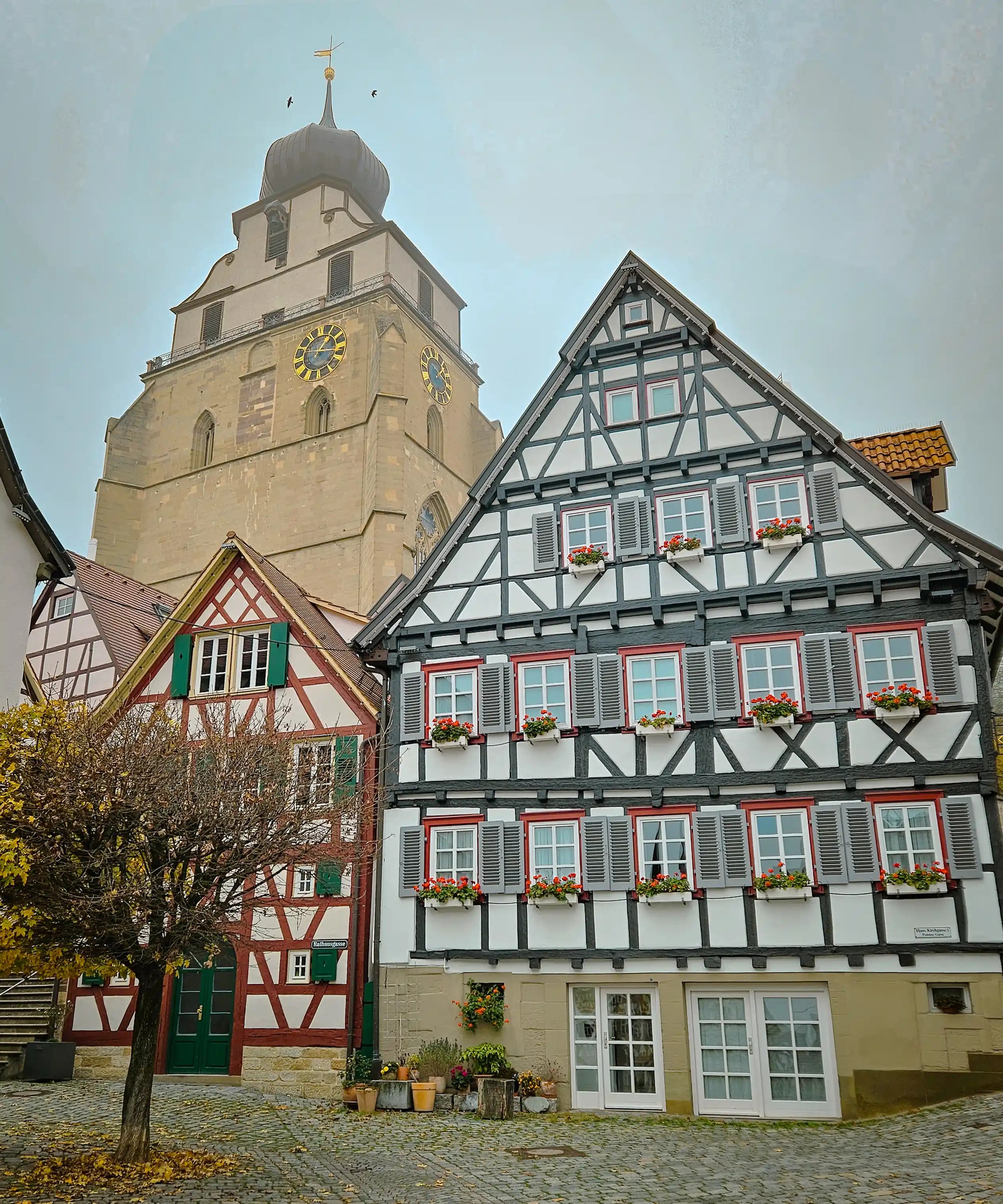 Row of half-timbered houses with flower boxes beneath the Stiftskirche Herrenberg tower.