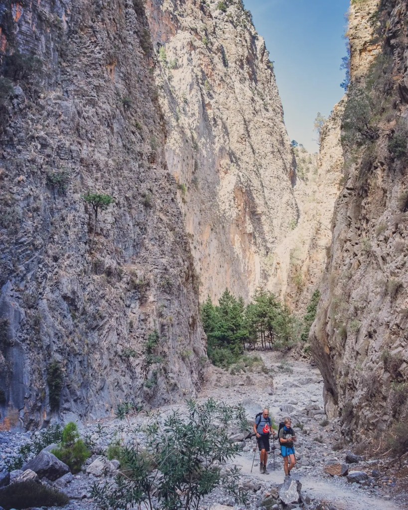 Two hikers walking along a rocky path between tall canyon walls in the gorge.